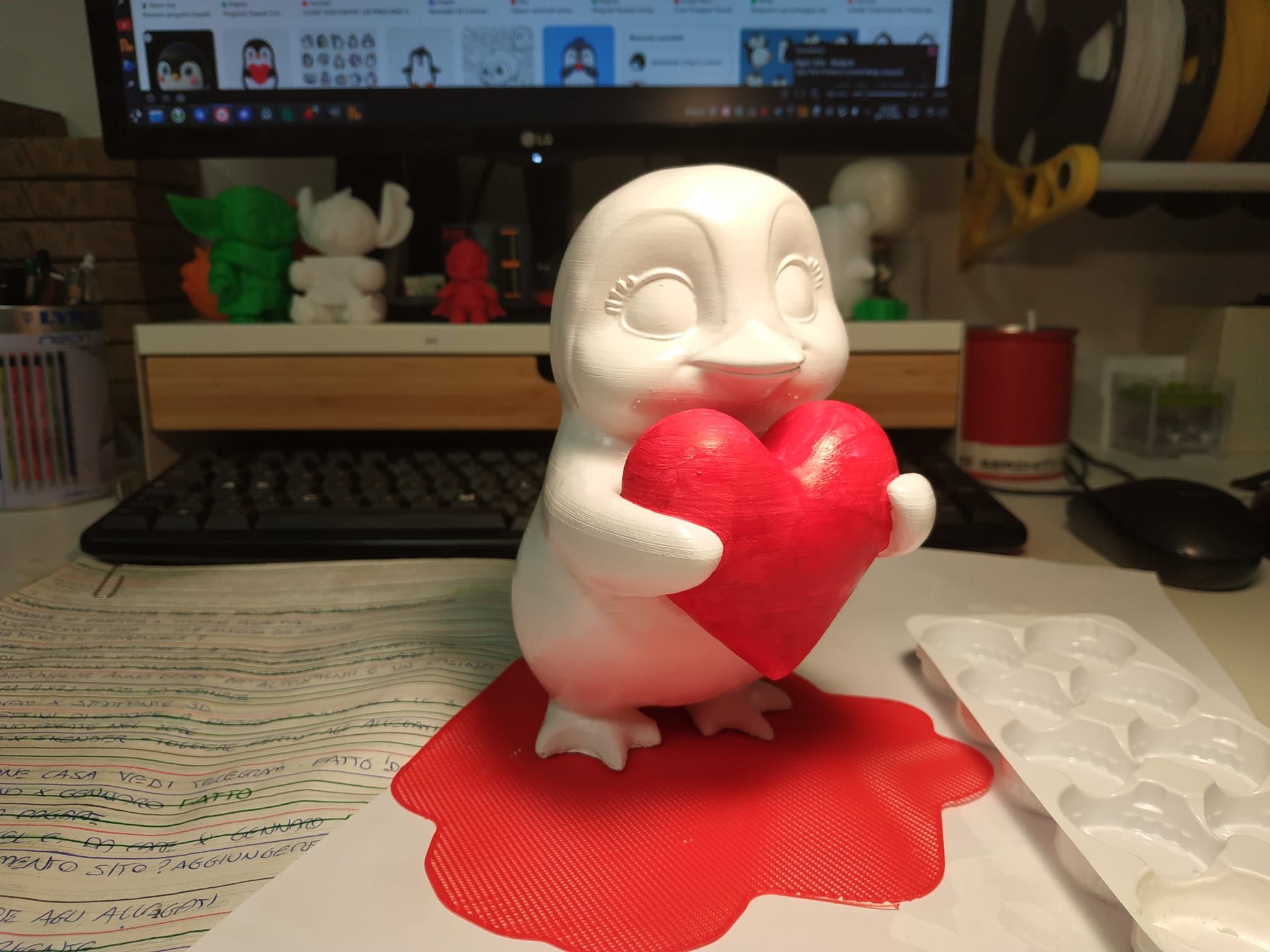 Foto di un pinguino che abbraccia un cuore rosso, l'unica cosa colorata al momento, il resto è bianco.
Scrivania disordinata sullo sfondo.