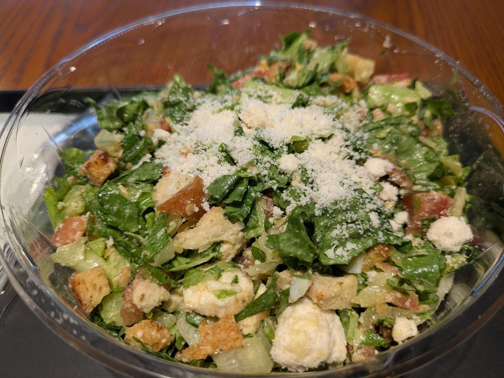 A plastic bowl filled with grilled chicken Caesar salad