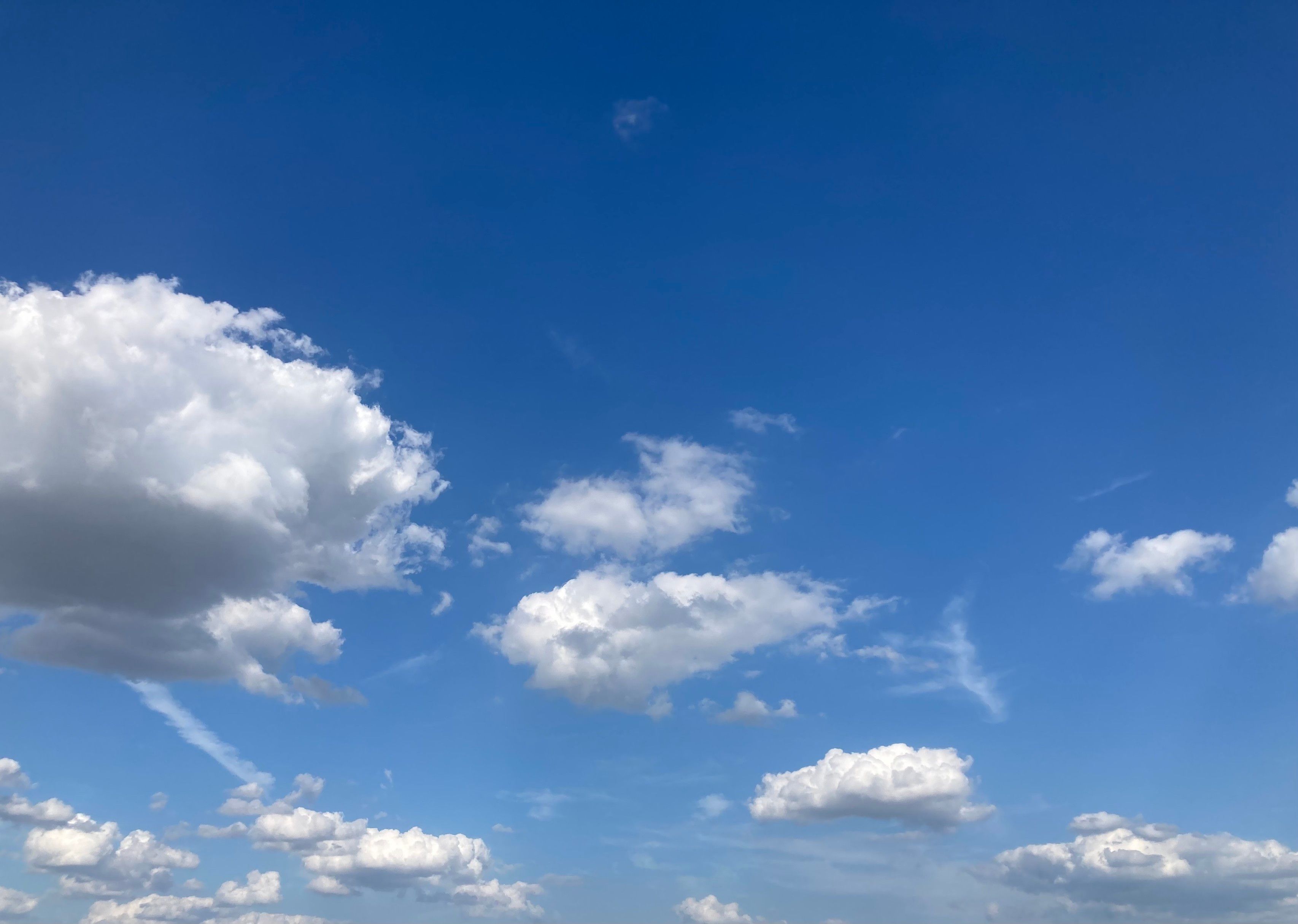 Weiße Wolken am blauen Himmel. Von links nach recht haben sich kleine Ausläufer zur jeweils nächsten Wolke gebildet. Eine dünne Wolke ähnelt vom Umriss einer Person, die eilig auf eine Wolke zuläuft.