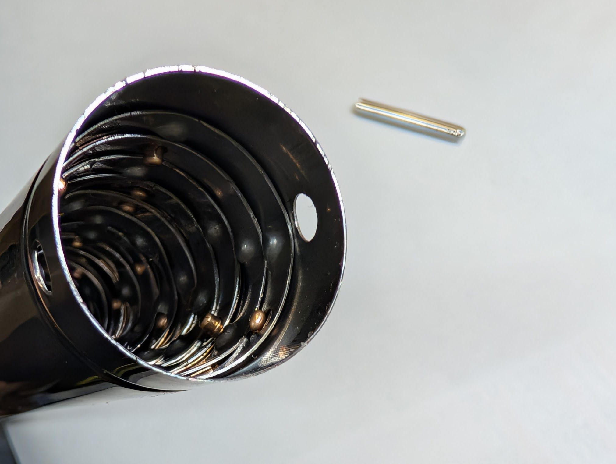 A view into the bottom end of a whip antenna, showing yellow metal tabs for better electrical connections between the concentric sleeves, stops preventing collapsing the antenna too far, and a set of holes. An out-of-focus roll pin is in the background.