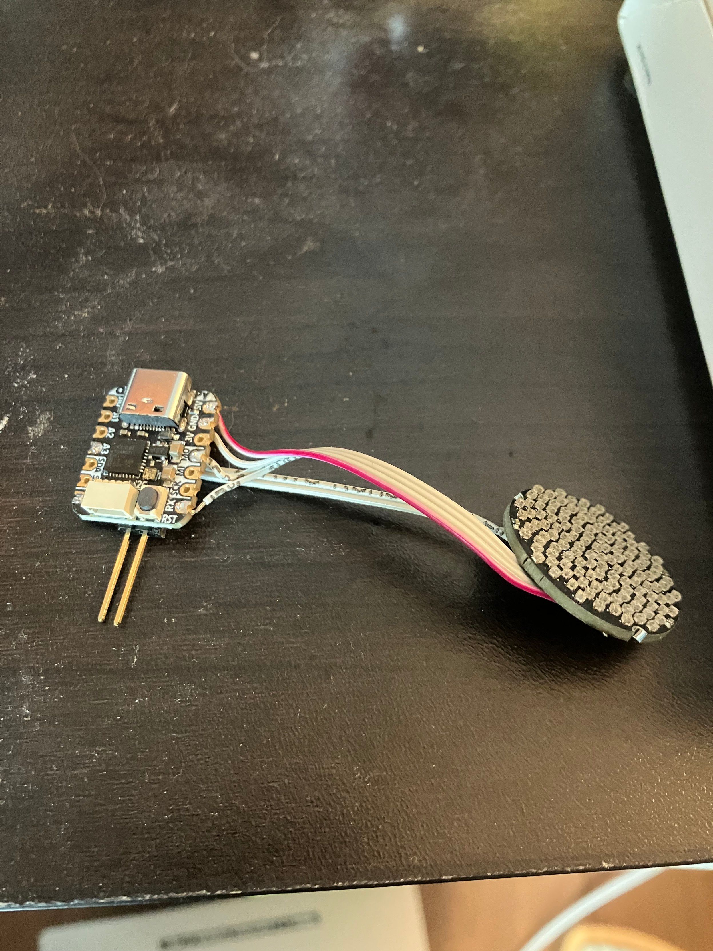 a microcontroller connected to an LED board with some ribbon cable. the microcontroller has two pins sticking far out of its profile, too.