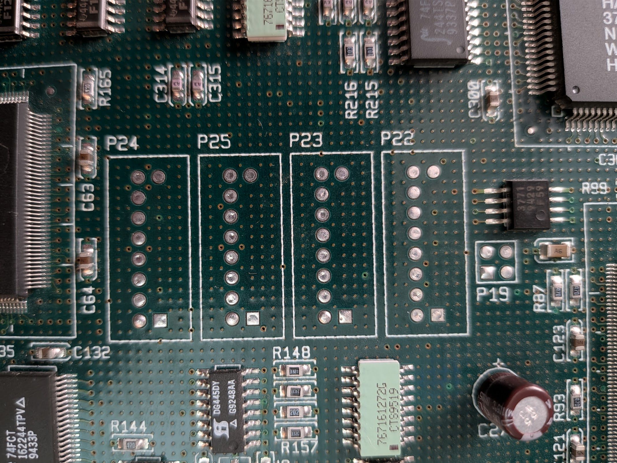 Photo of a circuit board with some unpopulated test ports.  They're each 2x8 pin arrangements with one row of 8 drilled, and only the first and last pin of the second row drilled.  All the drills are filled with solder, and one of the corners on the sparse row is square instead of circular. Each port has a silks border around it big enough for a 4x8 or maybe 5x10 header, suggesting a plastic housing.
