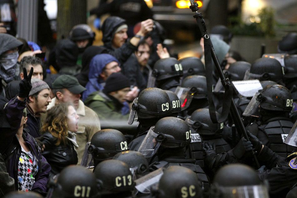 A photograph showing heavily armored police pepper-spraying protesters who are seated with their arms linked, during the Occupy movement of 2011.