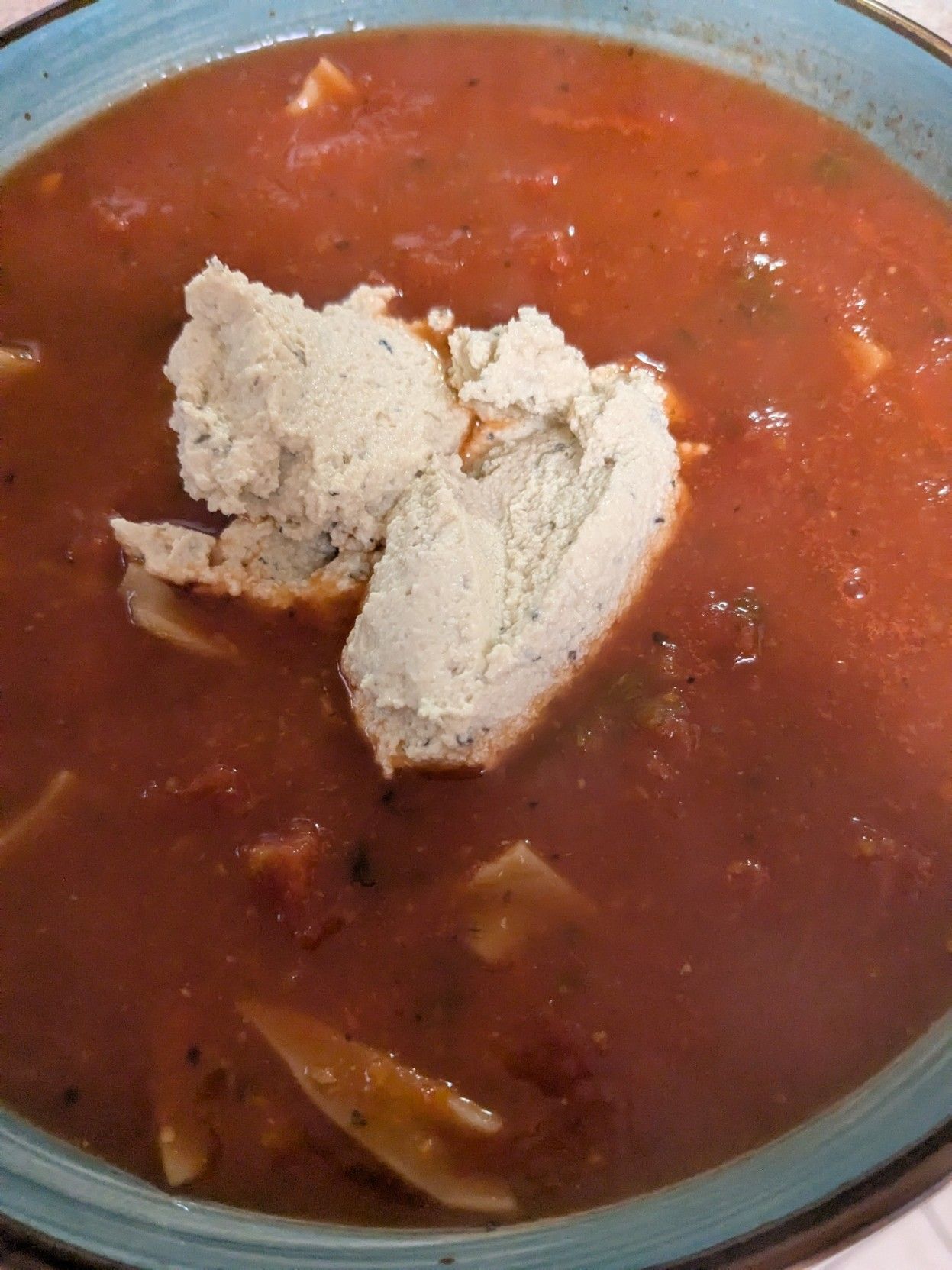 A bowl of rich looking tomato soup with a large dollop of fake ricotta in the middle