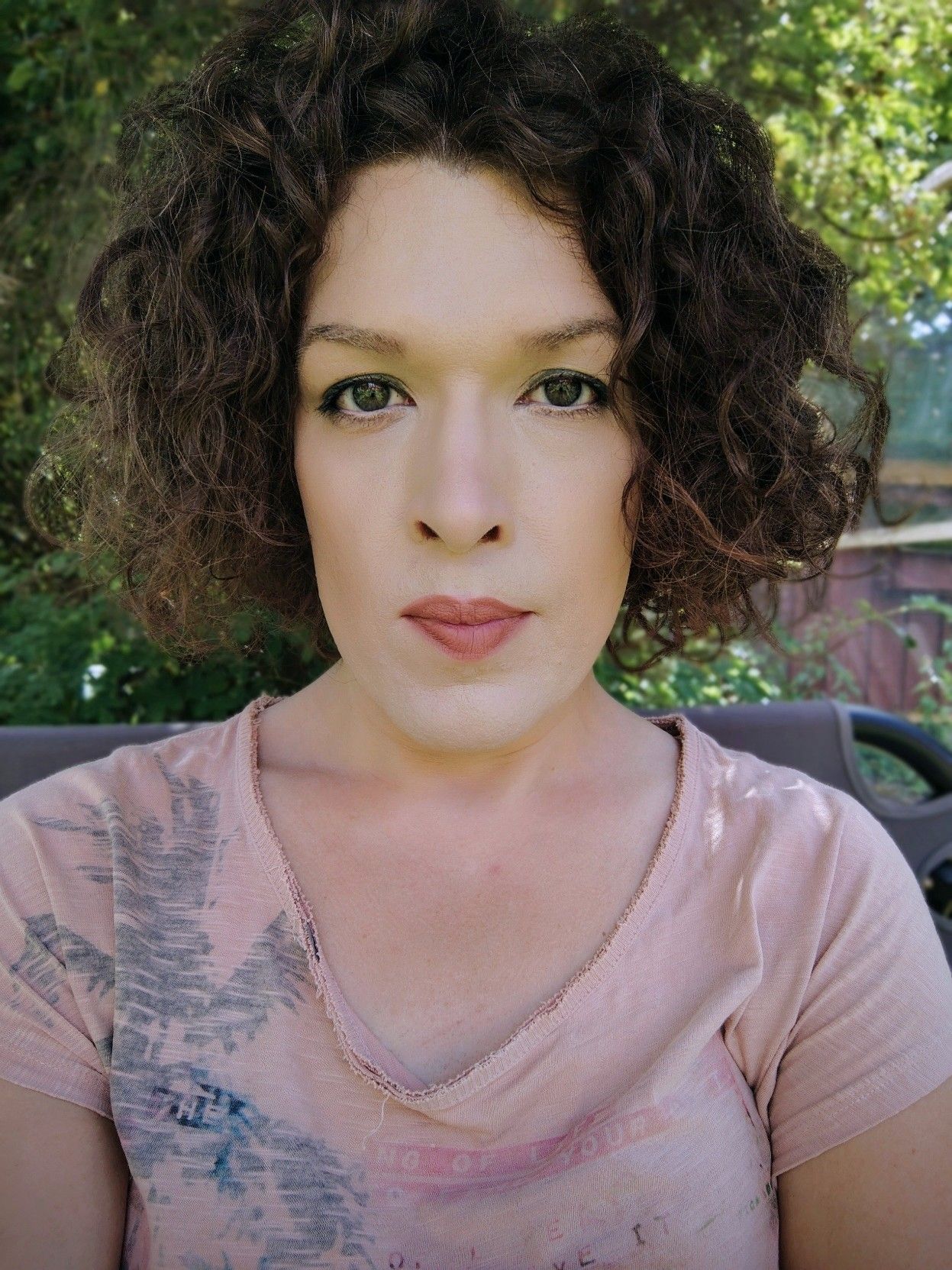 selfie, sitting in the garden smirking to the camera, it is summer, wearing an orange–pink top