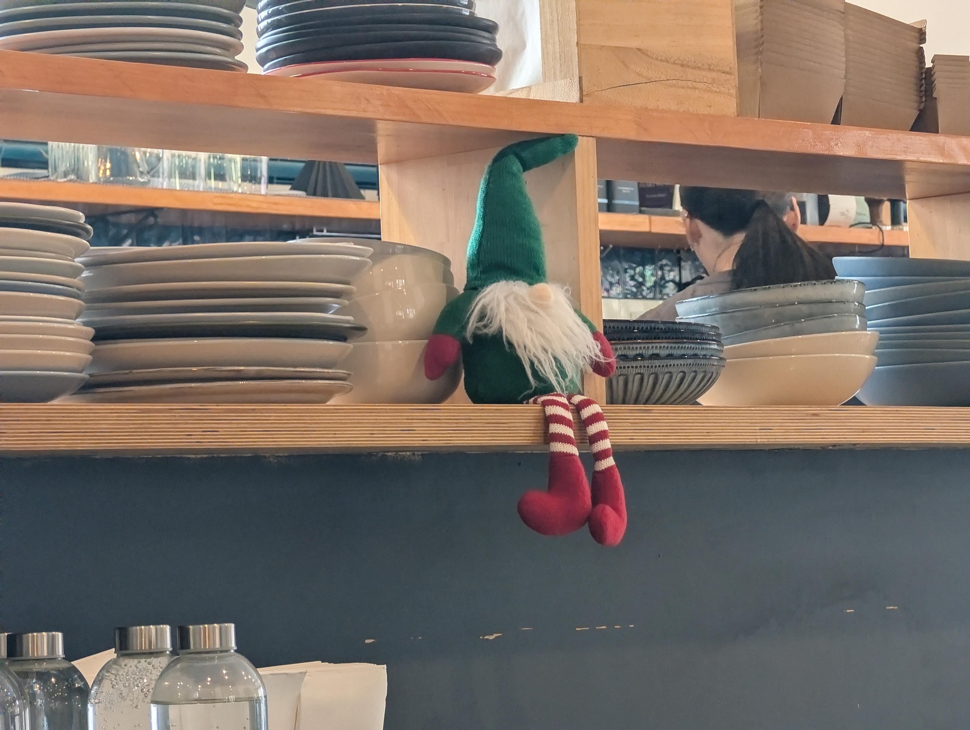 A stuffie elf sitting on the shelf with a heap of plates