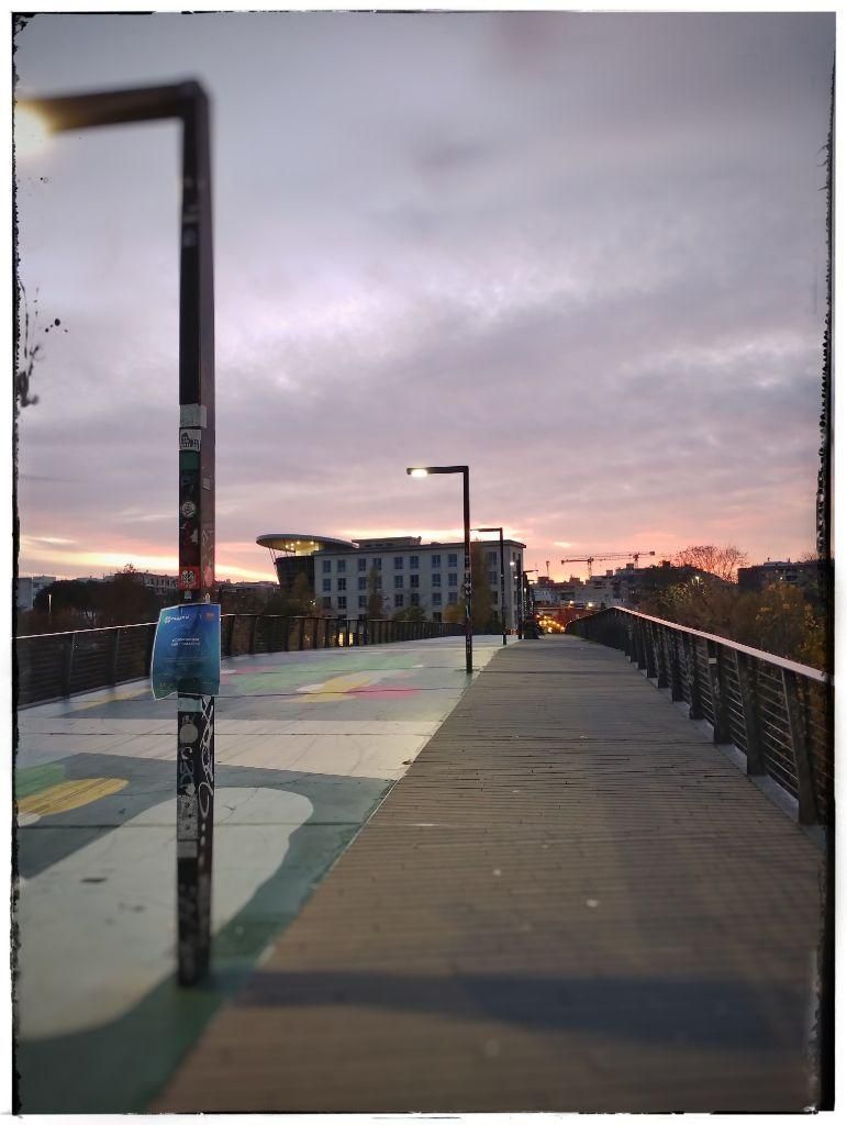 Fotografia presa su un ponte pedonale con sullo sfondo degli edifici e il cielo al tramonto
