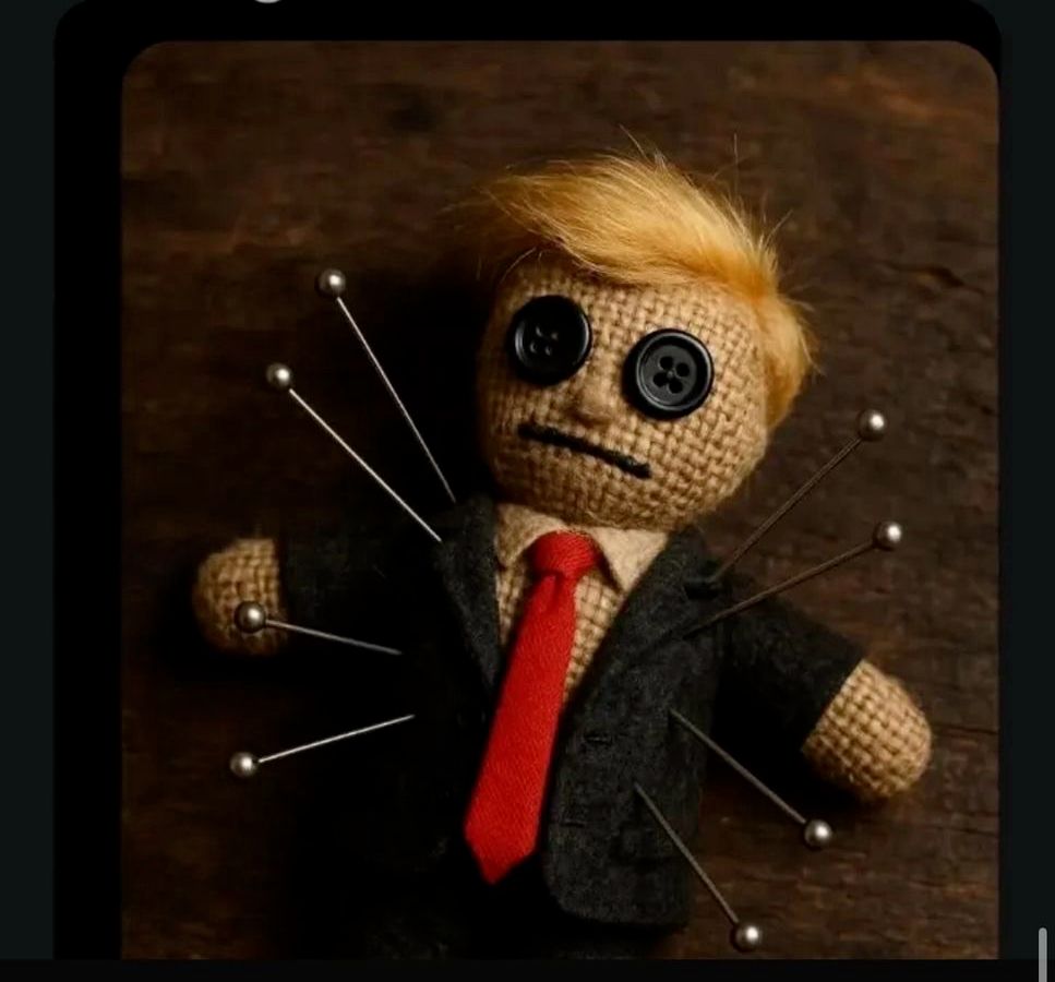 A voodoo doll that looks like Donald J Puppyfucker, with a lock of hair, red tie, and button eyes, has several pins jabbed into it.