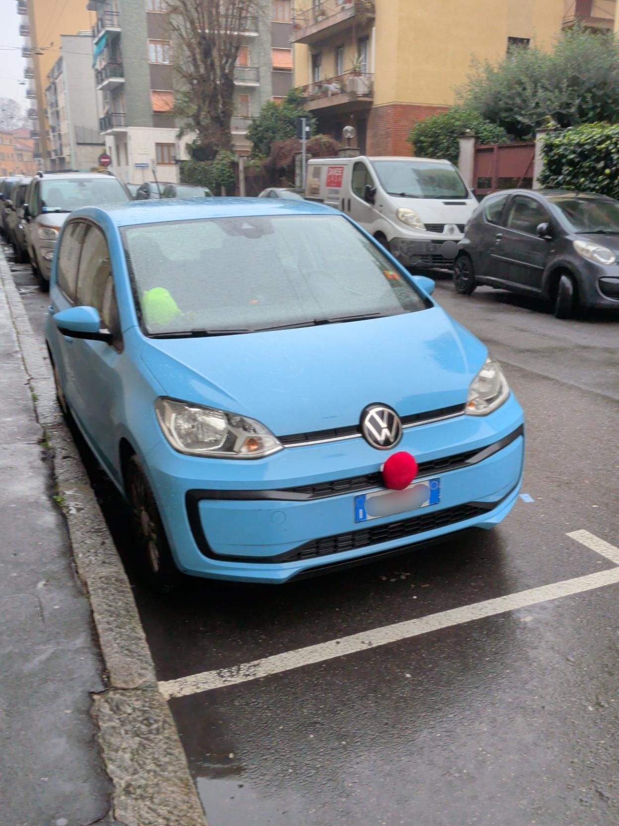 Auto azzurra con un naso rosso, parcheggiata vicino a un marciapiede