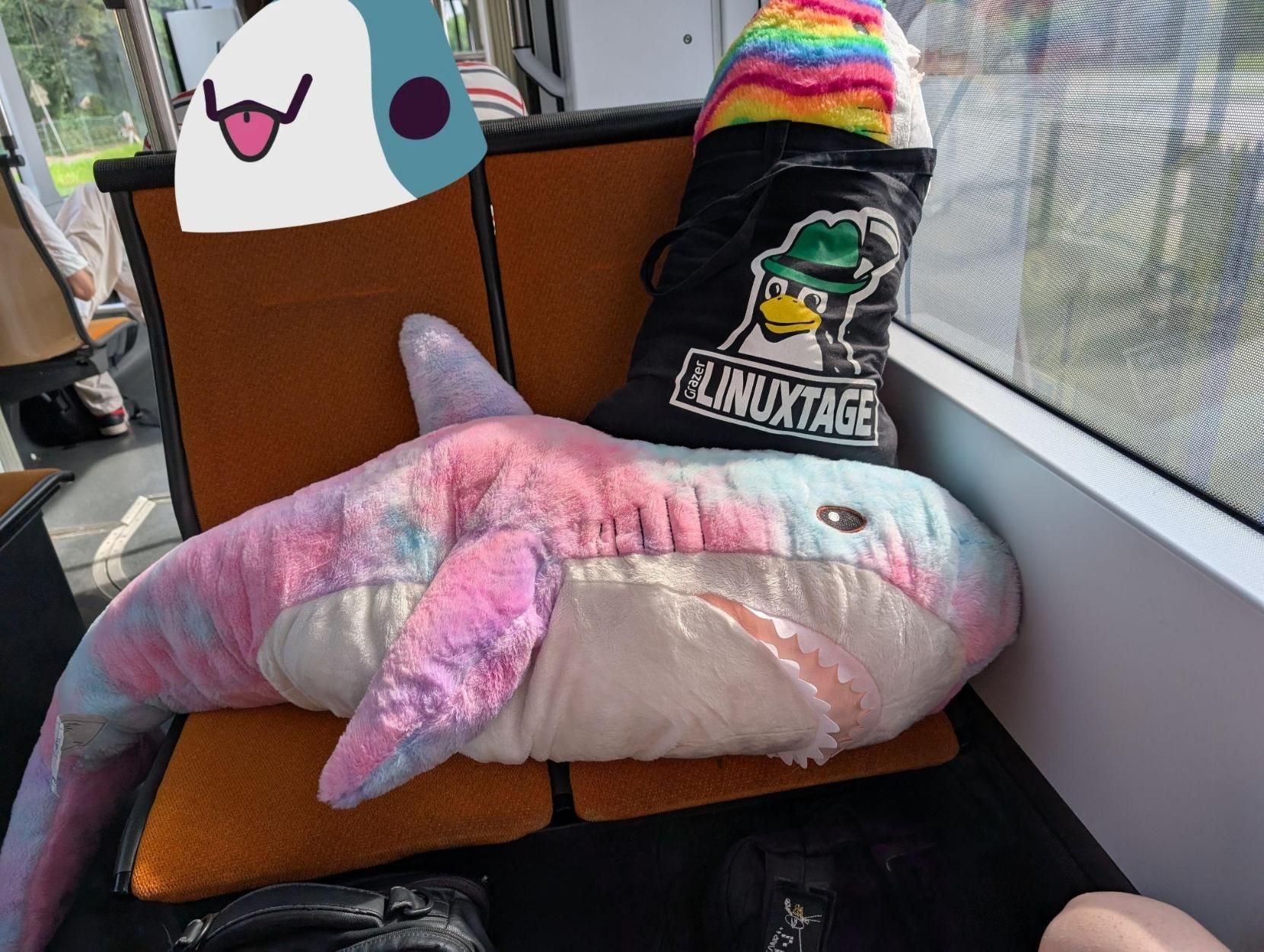 Two Blåhajs on tram seats; a very large one is covering two seats, and a large one is stuffed into a fabric bag