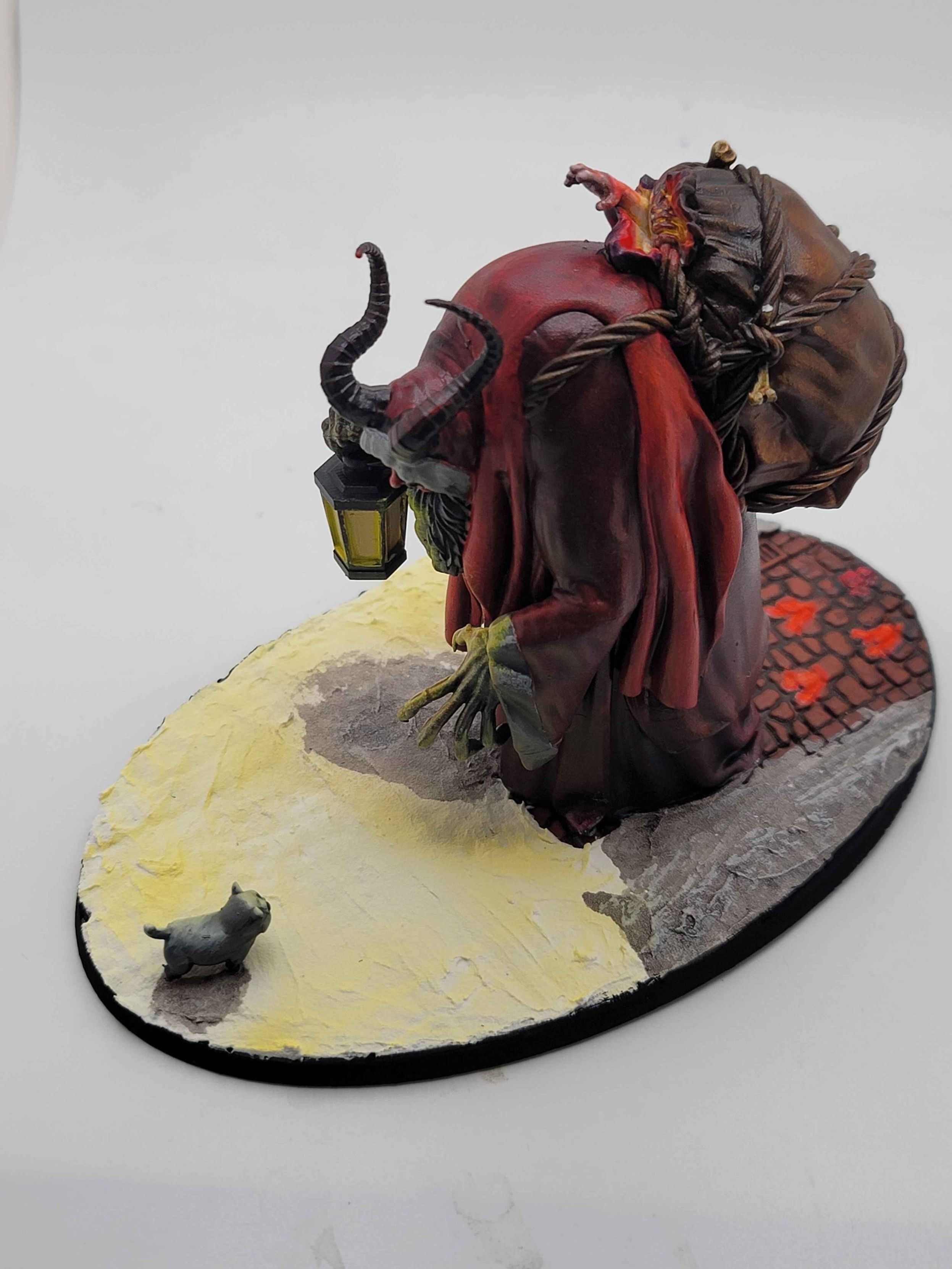 A high quarter angle on the diorama, showing the hellish light coming from the inside of the child bag, as well as the yellow light lighting the upper face of the cat confronting Krampus.   From this angle it's easier to see the cuff on Krampus's left wrist lit yellow by the lantern.