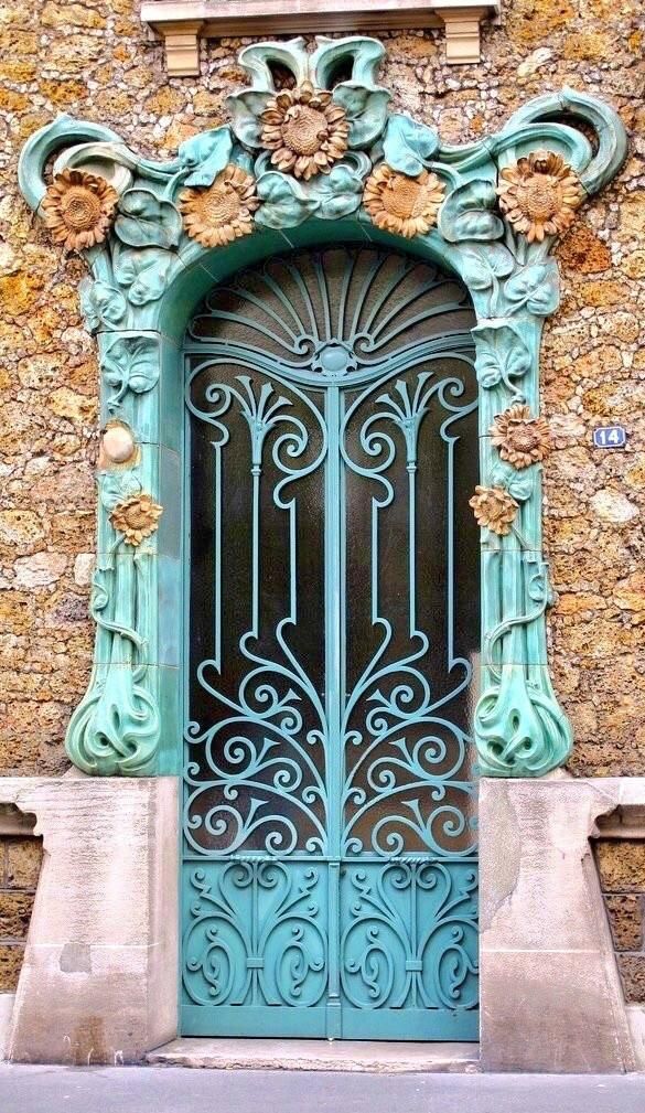 A turquoise art bouveau door featuring brown-orange ornate floral motifs and a wrought-iron gate. 