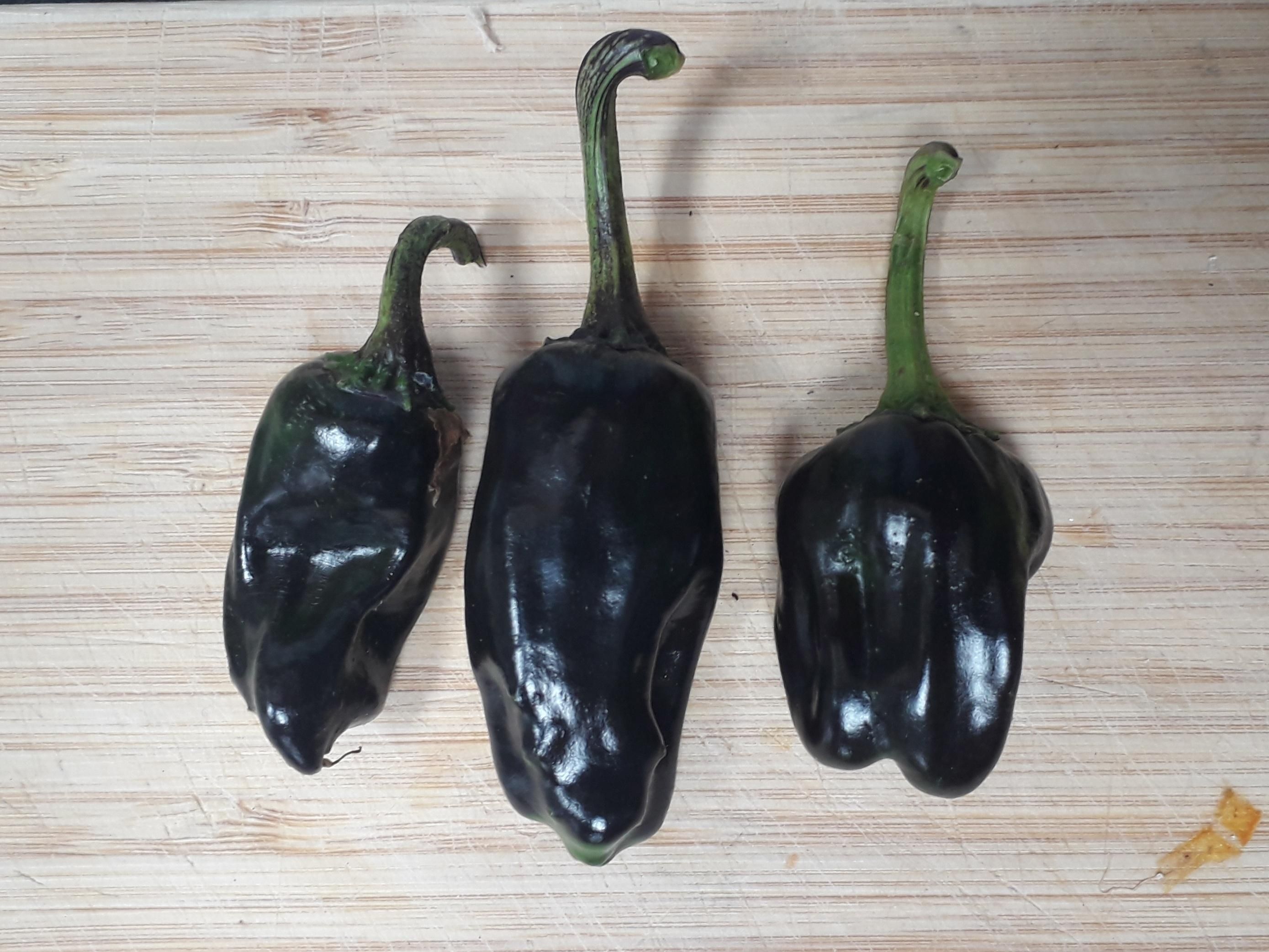 Three black chillies on a wooden chopping board.