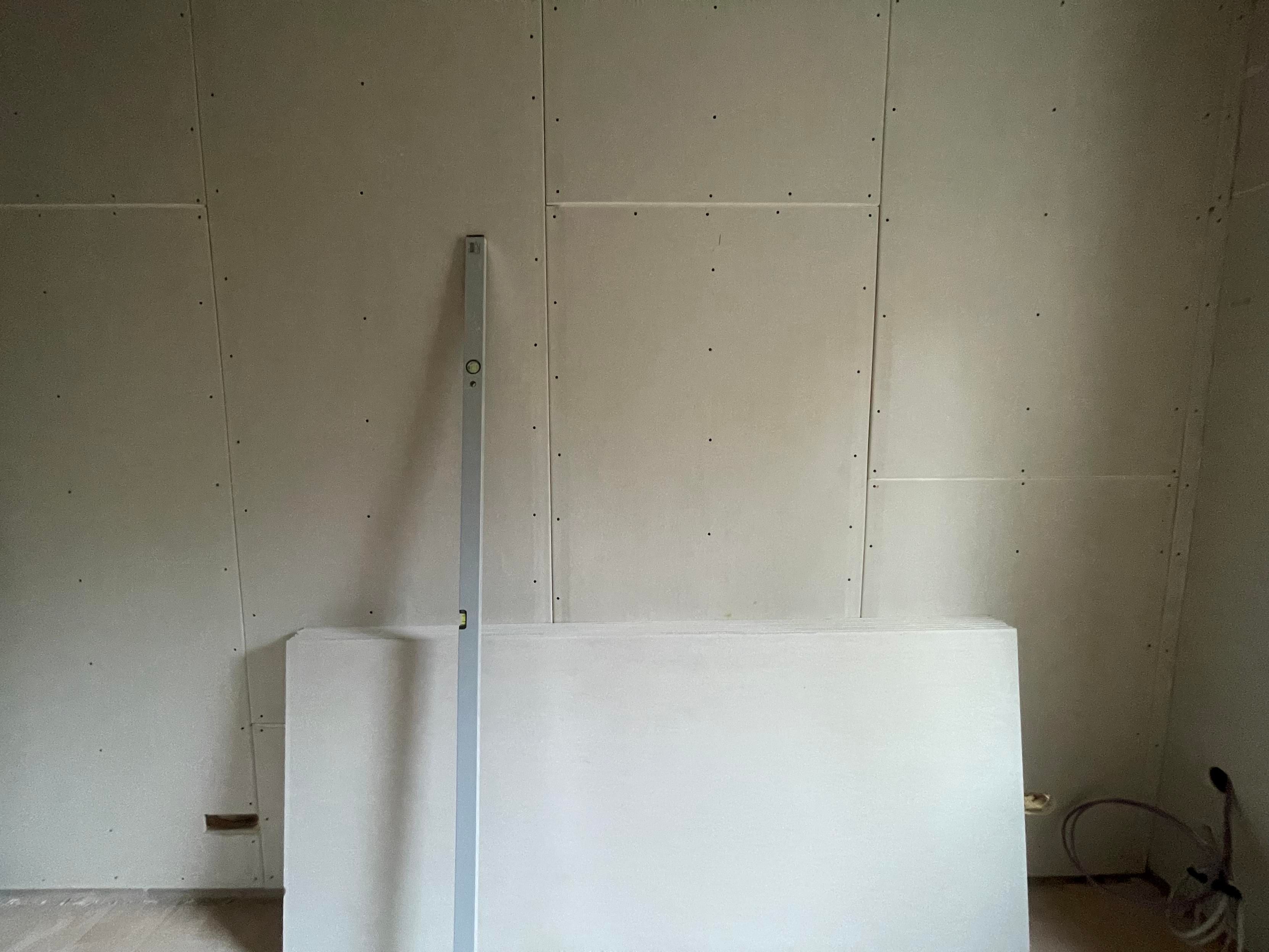 Plain plasterboard fixed to a wall. Some standing unused on the floor. 