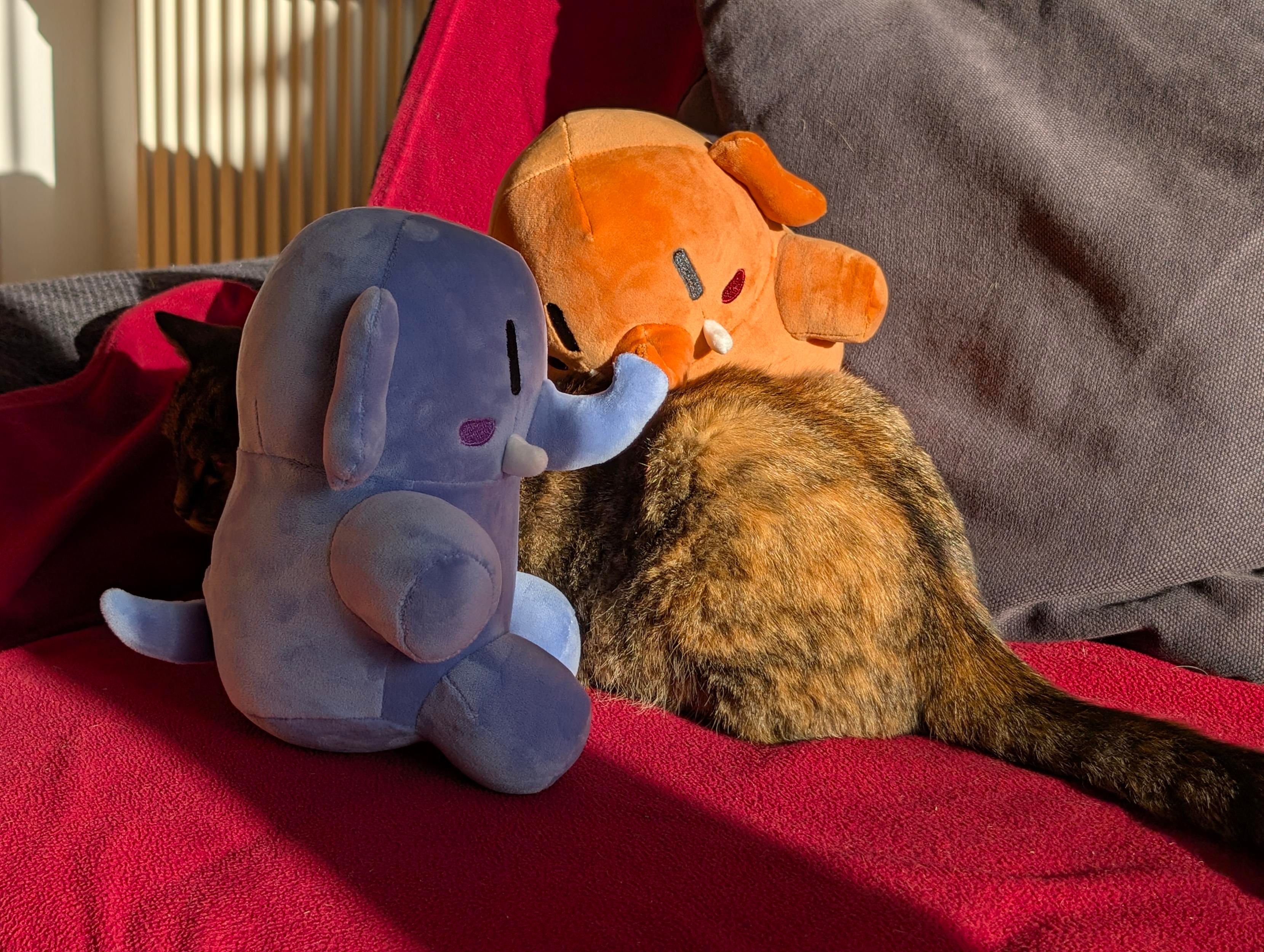 Same as photo 1, but the cat has turned her back away from the viewer, while the plushtodons are facing the cats' body looking very busy with their hands