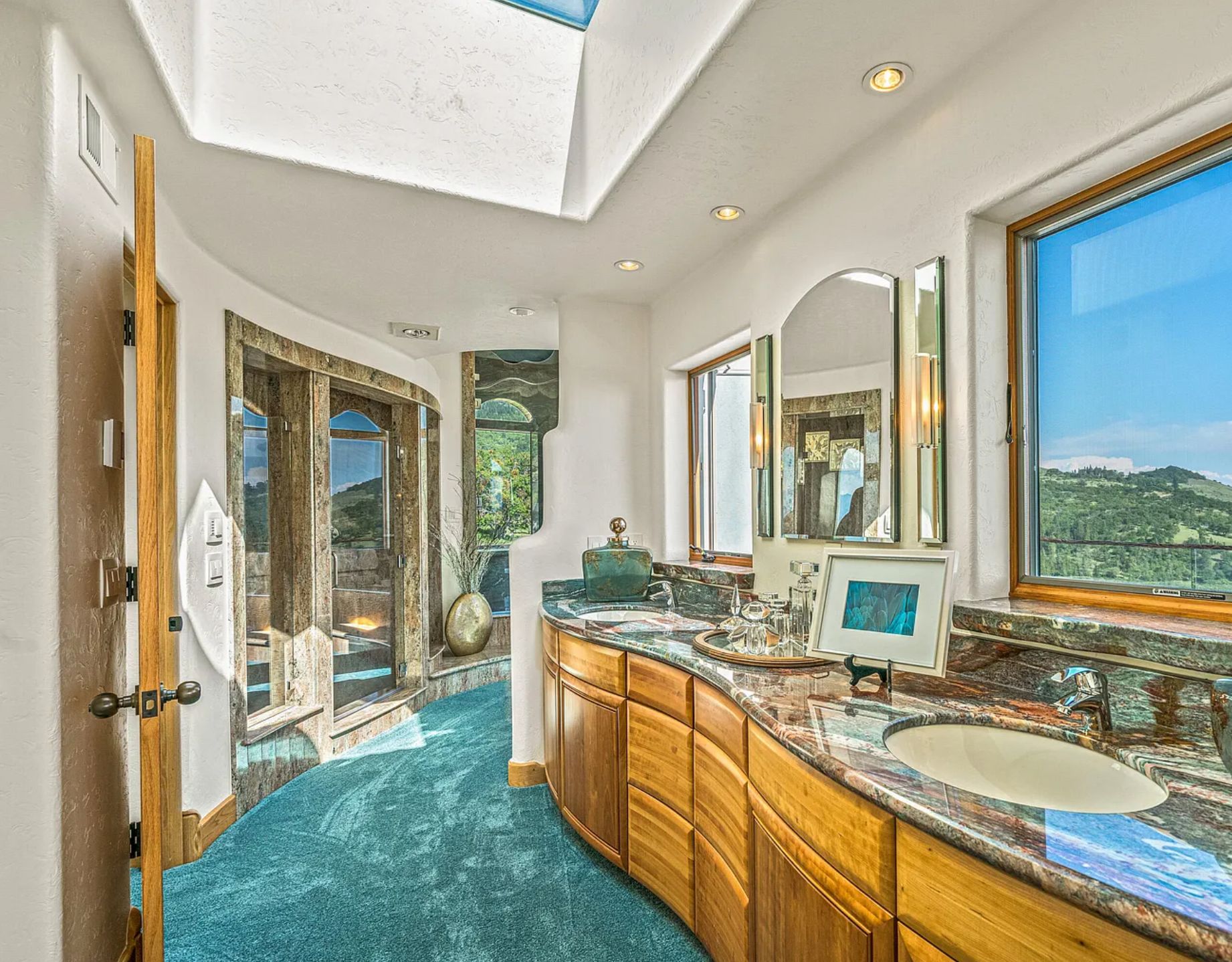 A very large bathroom with a curving wood vanity with marble top, and teal coloured plush carpet on the floor. 