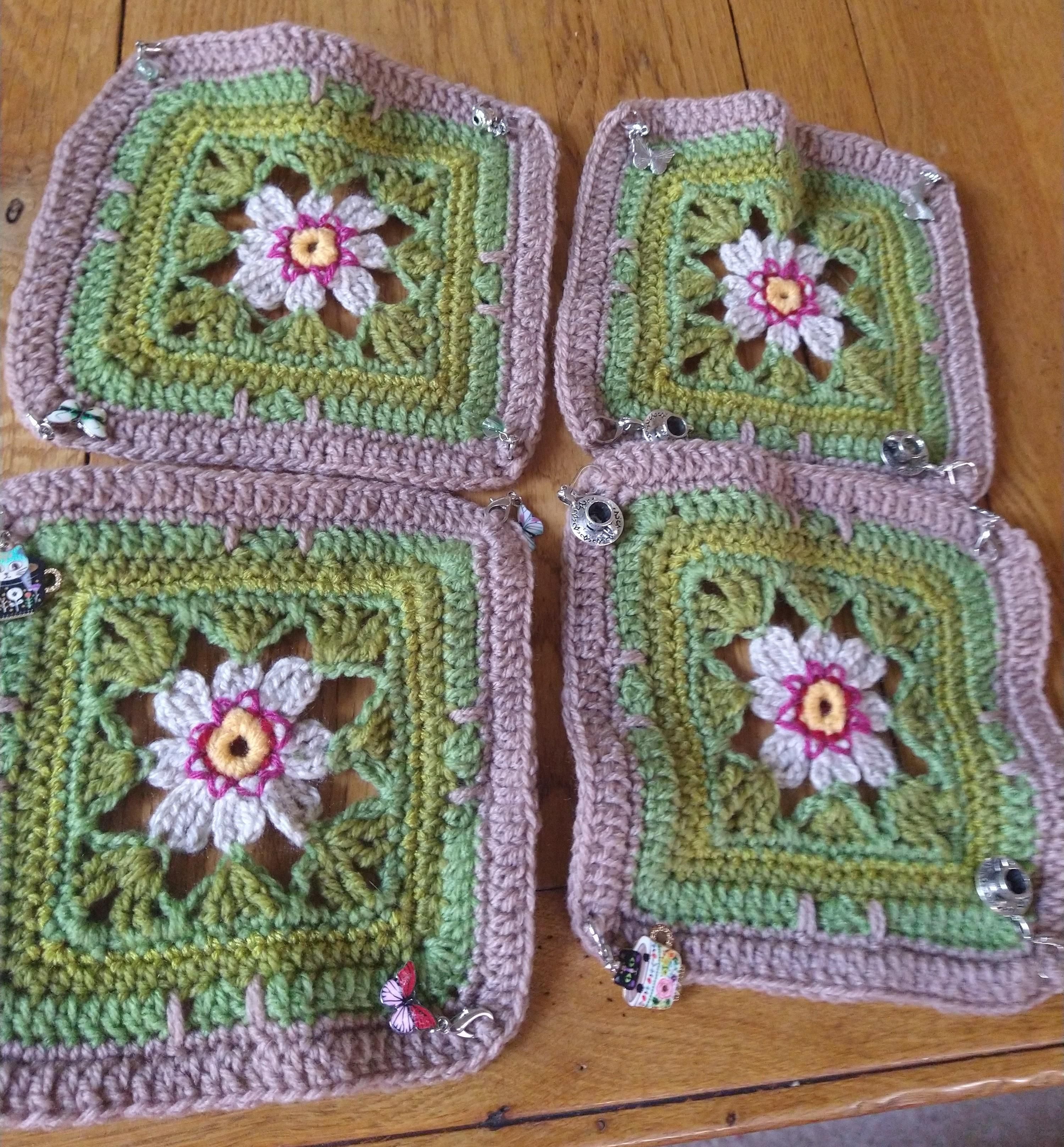 Four  complete crochet square motifs in green and beige with stitch markers in the corners 