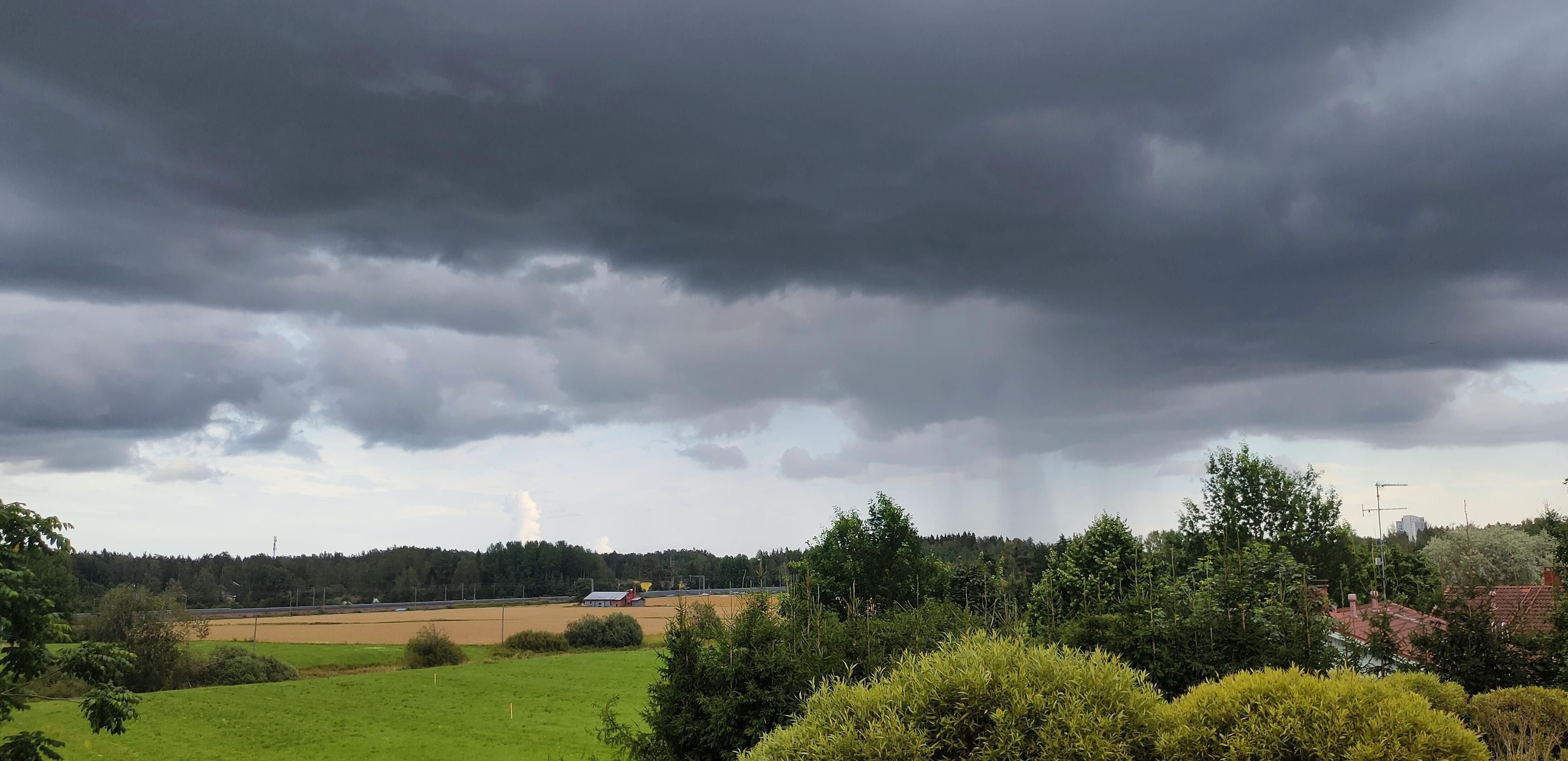 Black low clouds in mid-distance over an open landscape, a colum of rain visible in horizon

Photo and view by me