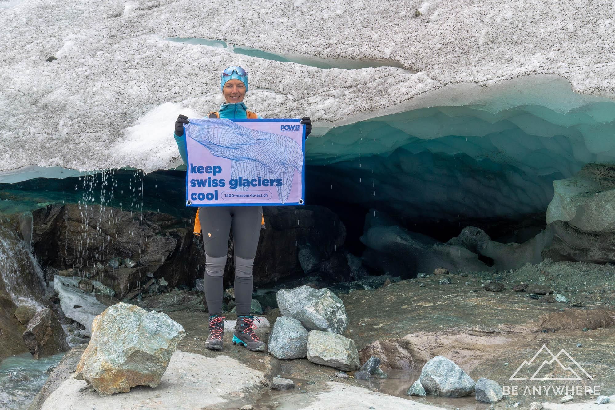 woman standing next to a melting glacier holding a flag saying "keep Swiss glaciers cool"