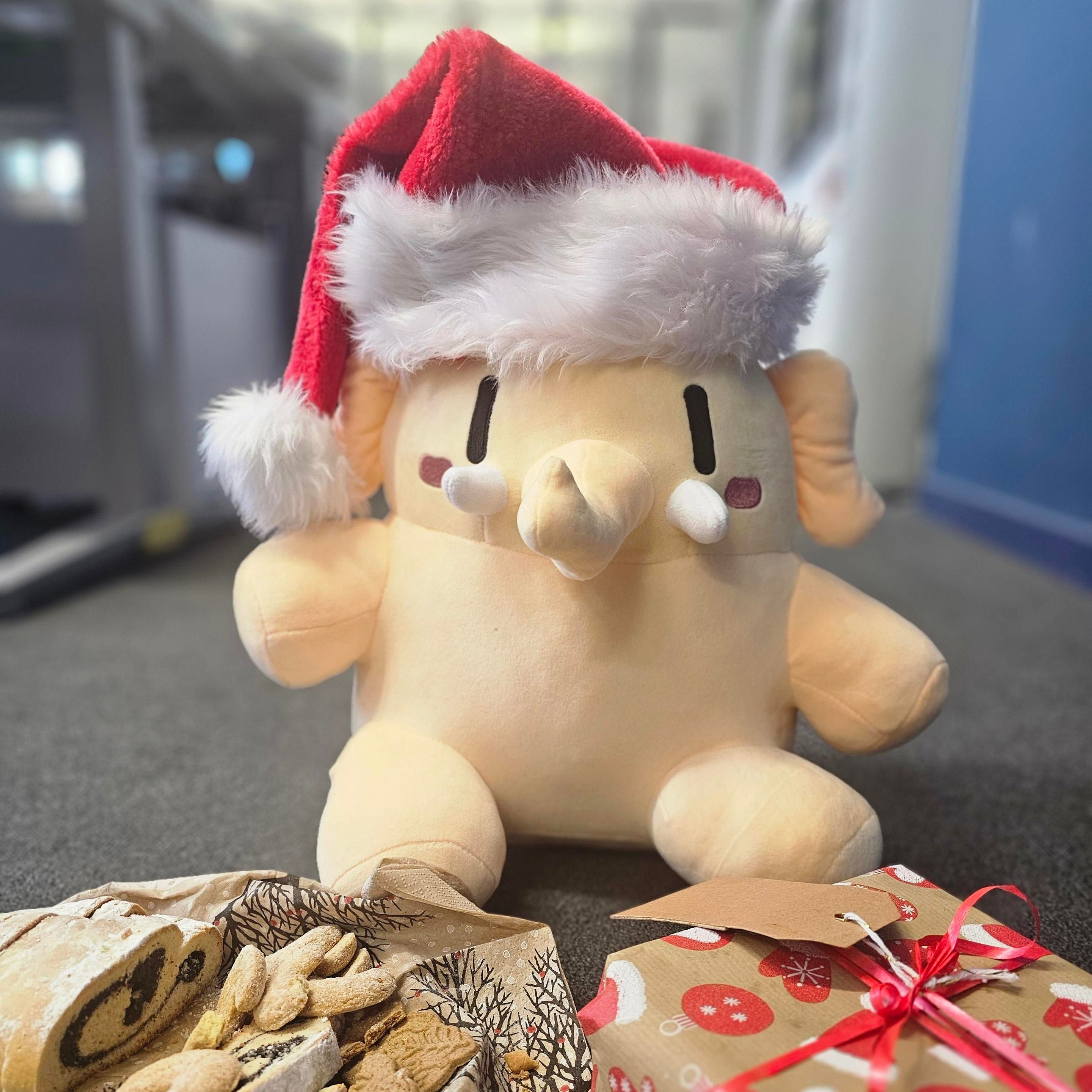 Das Mastodon-Mastkottchen hat eine Nikolaus-Mütze an und sitzt vor einem Teller mit Plätzchen und einem Weihnachtsgeschenk. 