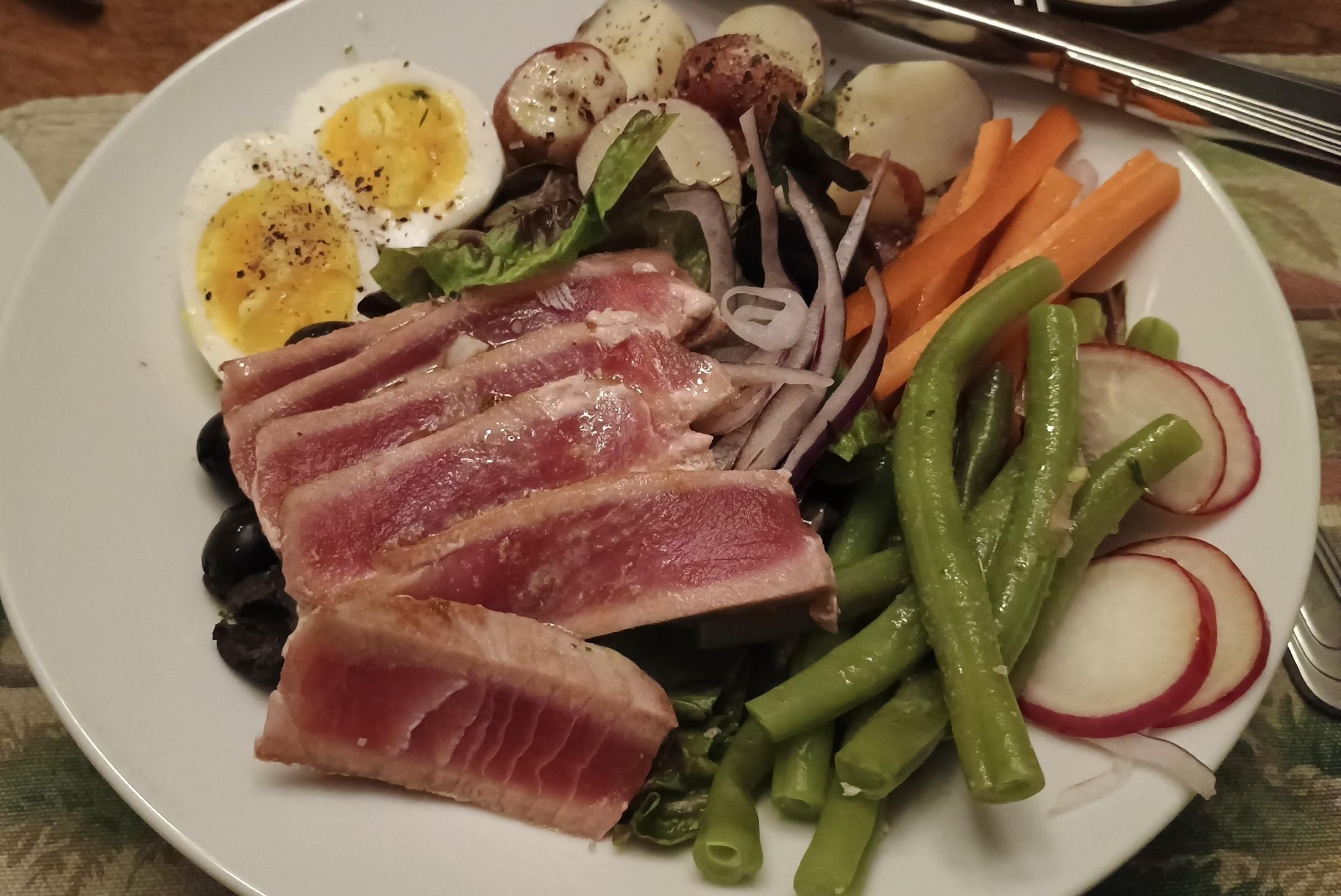 A Niçoise salad featuring garden potatoes, radishes, green beans, carrot and seared tuna steak, and a hard boiled egg. 