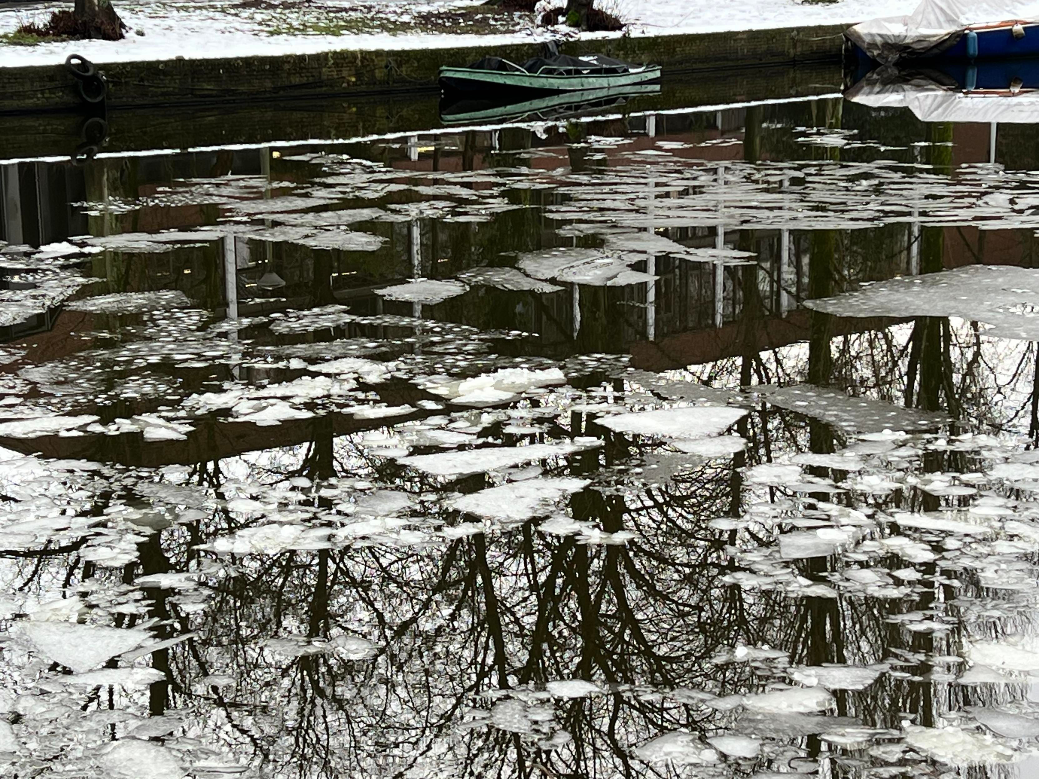 A canal with quite a bit of ice. Mostly monochrome but there is a green boat in the other side and a bit of green grass visible through the snow
