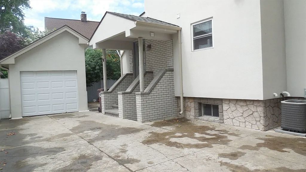 A side entrance to the house. There is a set of stairs going up to a door, with a brick wall on either side with a place to put your hand as you go up the stairs, like a banister. There is another 3rd one on the other wide and there is no door there. Then there is a garage that is a very odd shape, with what looks like part of a pitched roof chopped off. 