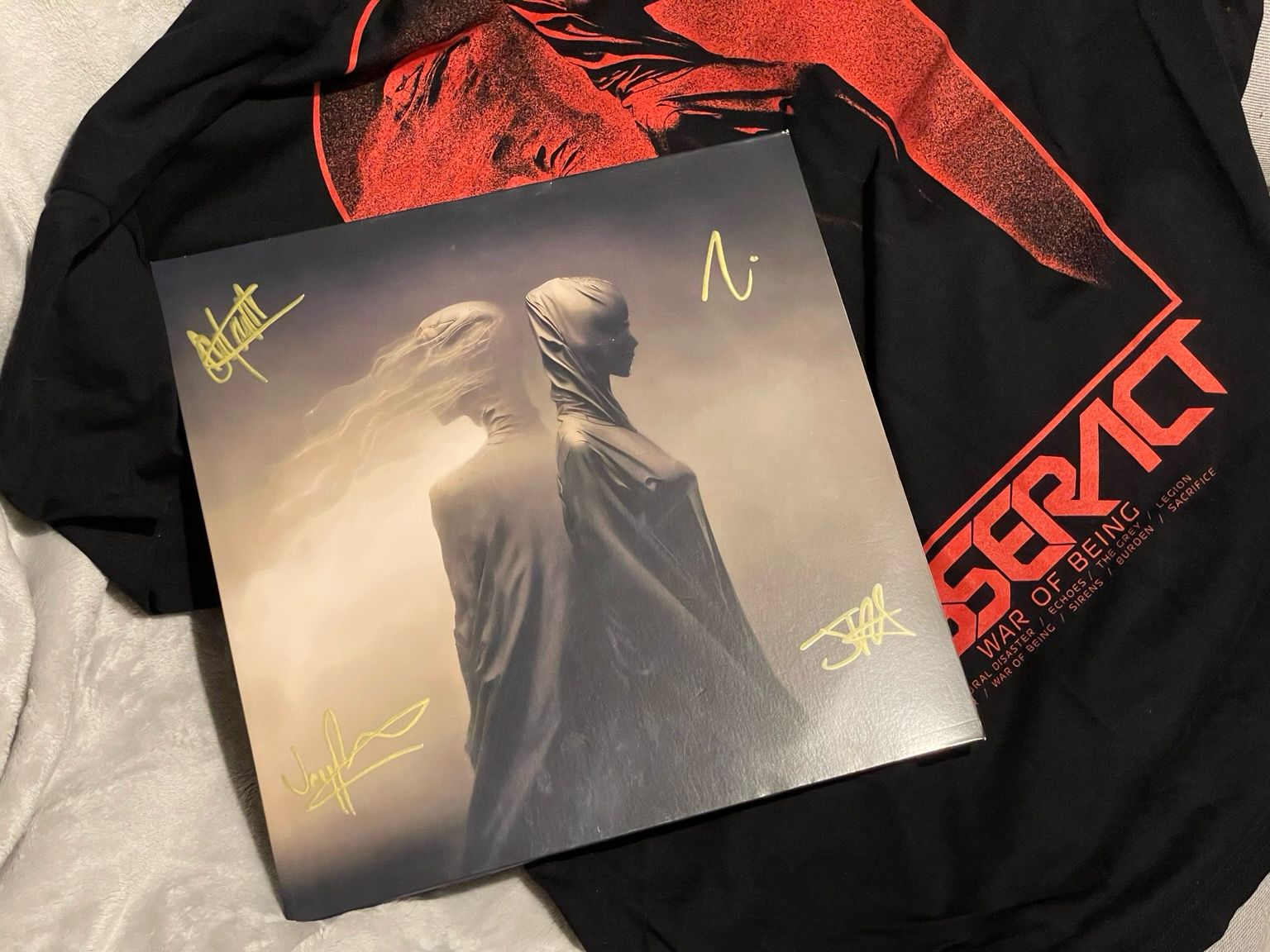 A War of Being LP sleeve with 4 signatures in golden marker, lying on top of a TesseracT War of Being t-shirt.