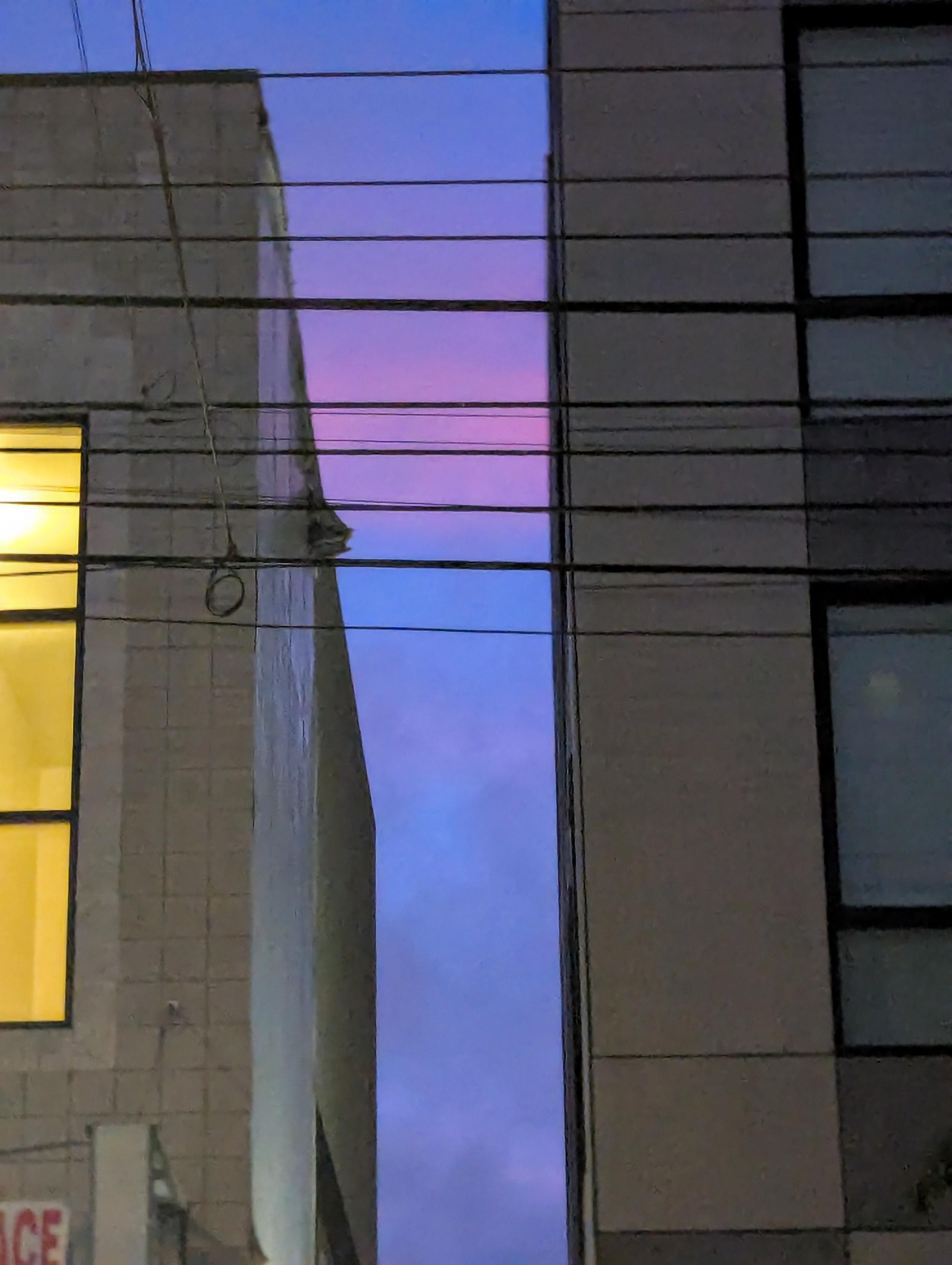 Blue, purple, pink clouds through a slit in buildings with a yellow kit window