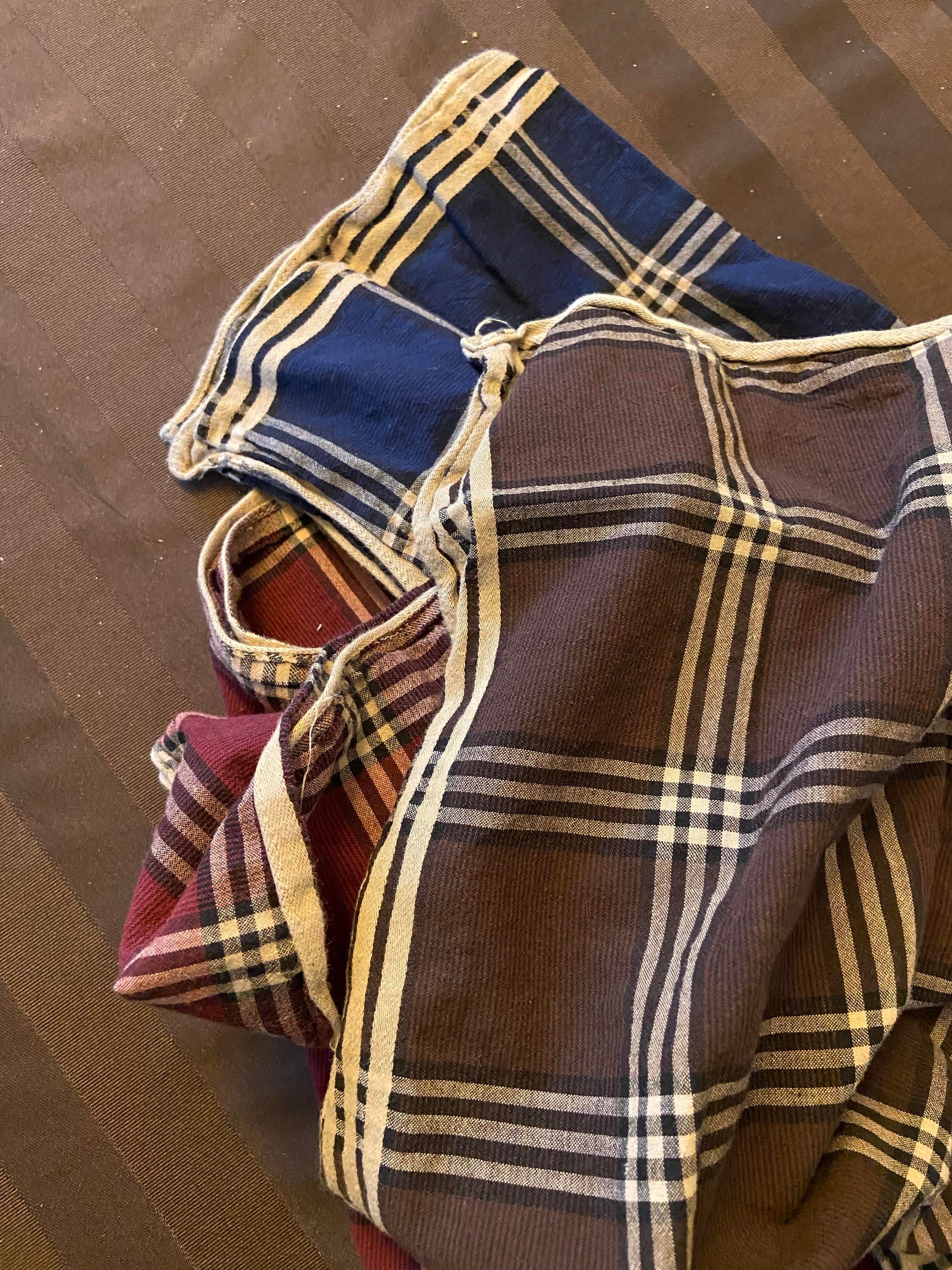 Some handkerchiefs, red, blue, and brown, with a beige checkered pattern. The edges are super wrinkly. If you folded these to put in your pocket, they would be super bulky because of the wrinkles. 
