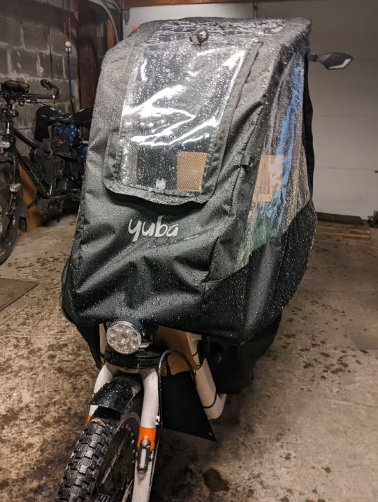 A wet Yuba Supermarche electric (converted) bakfiets with rain canopy, xtracycle in the background of an otherwise empty small garage