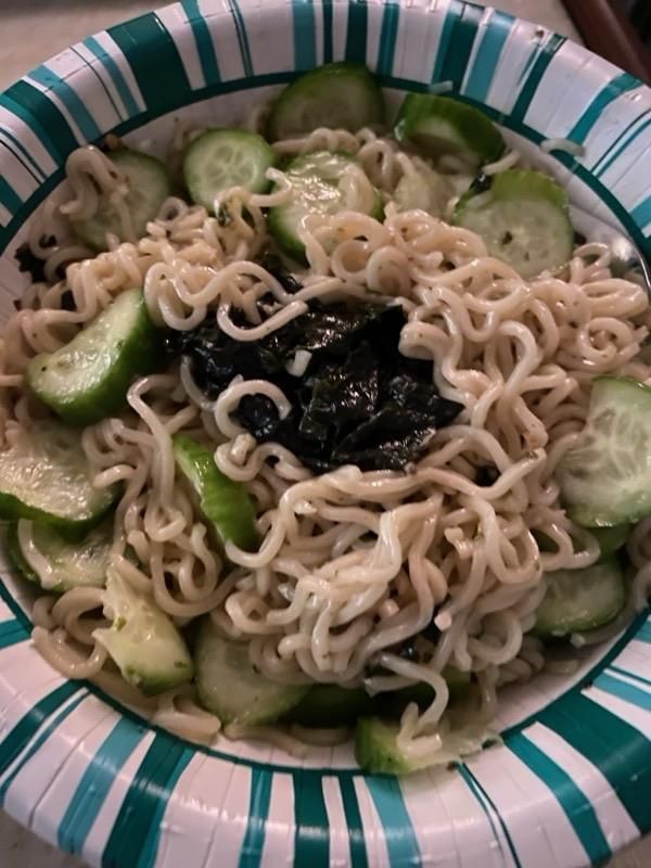 bowl filled with ramen and cucumber slices with a glob of seaweed in the middle