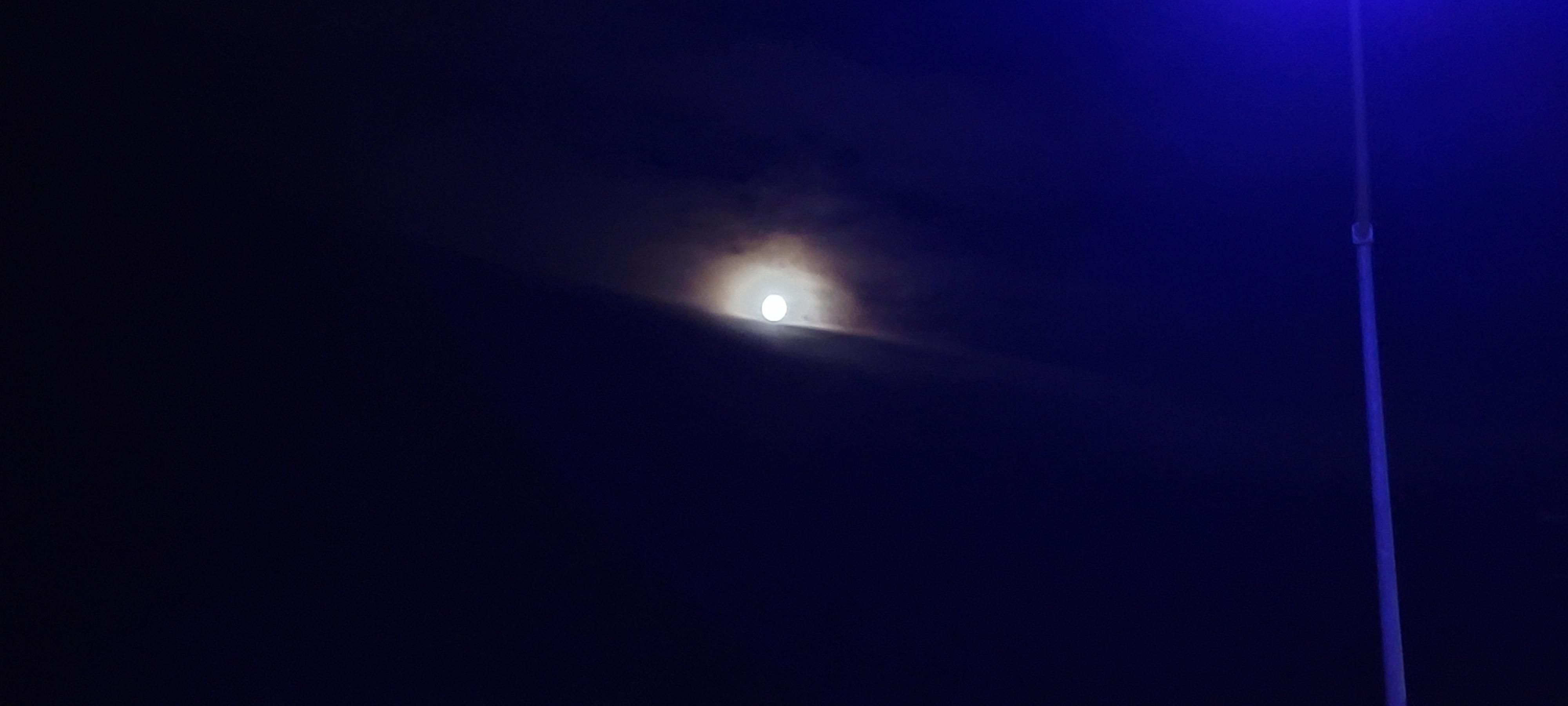 Moon partially obscured by clouds, with rainbow halo, pole of street lamp with lamp itself out of frame