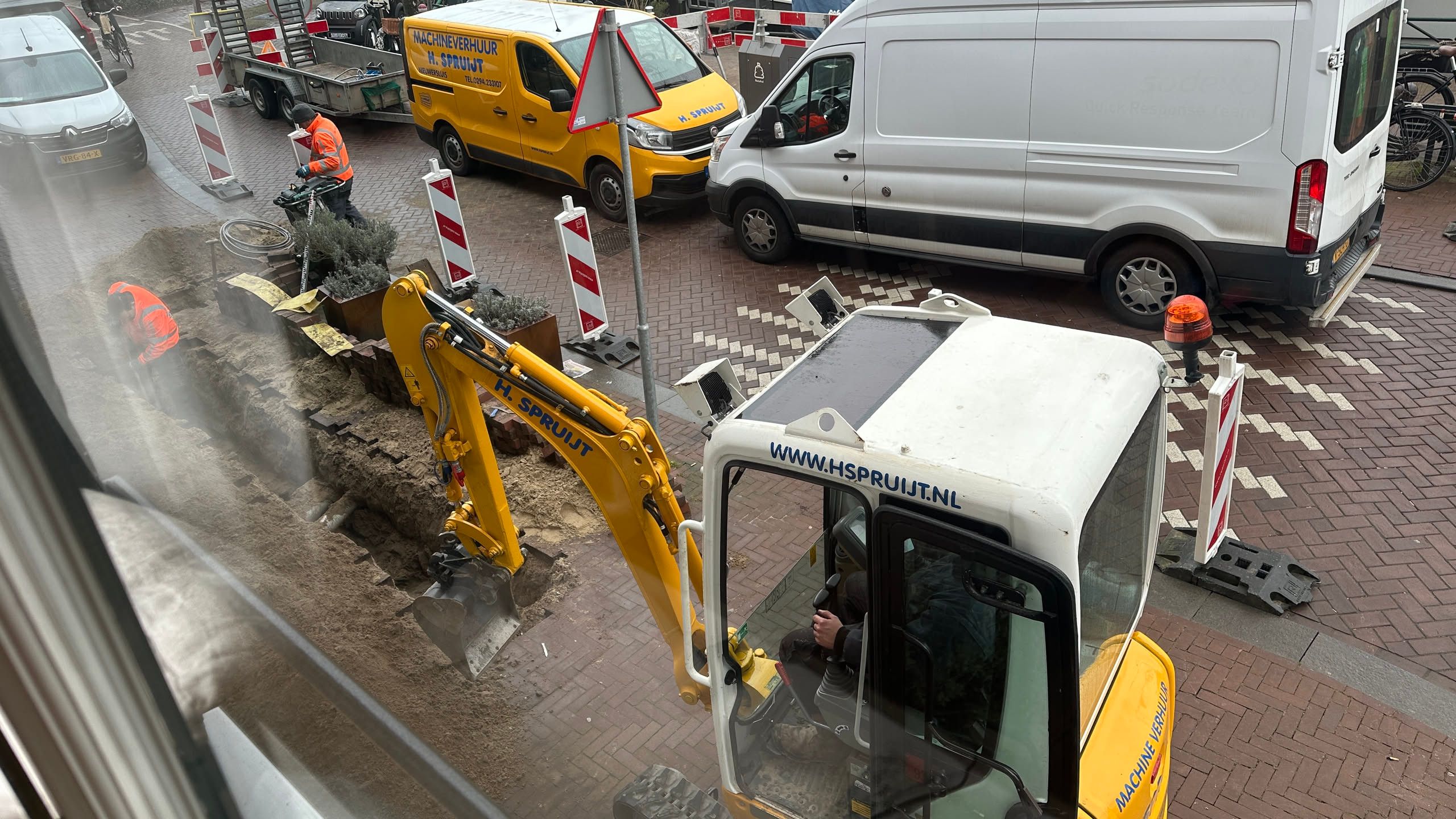 a small construction backhoe on a sidewalk, digging a trench in the bricks