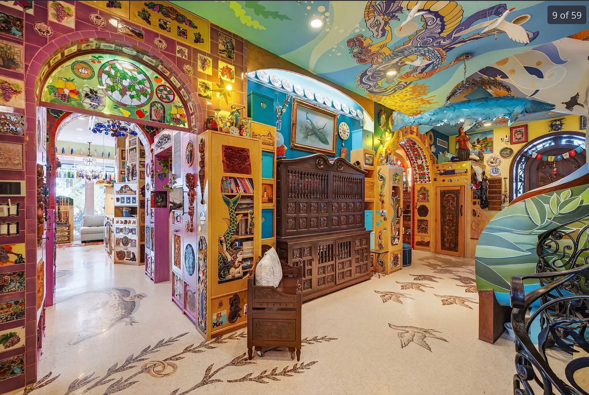 Another view of the living area also covered in bright patterns and murals, there is also stained glass above a doorway arch, and tiles on the wall. 