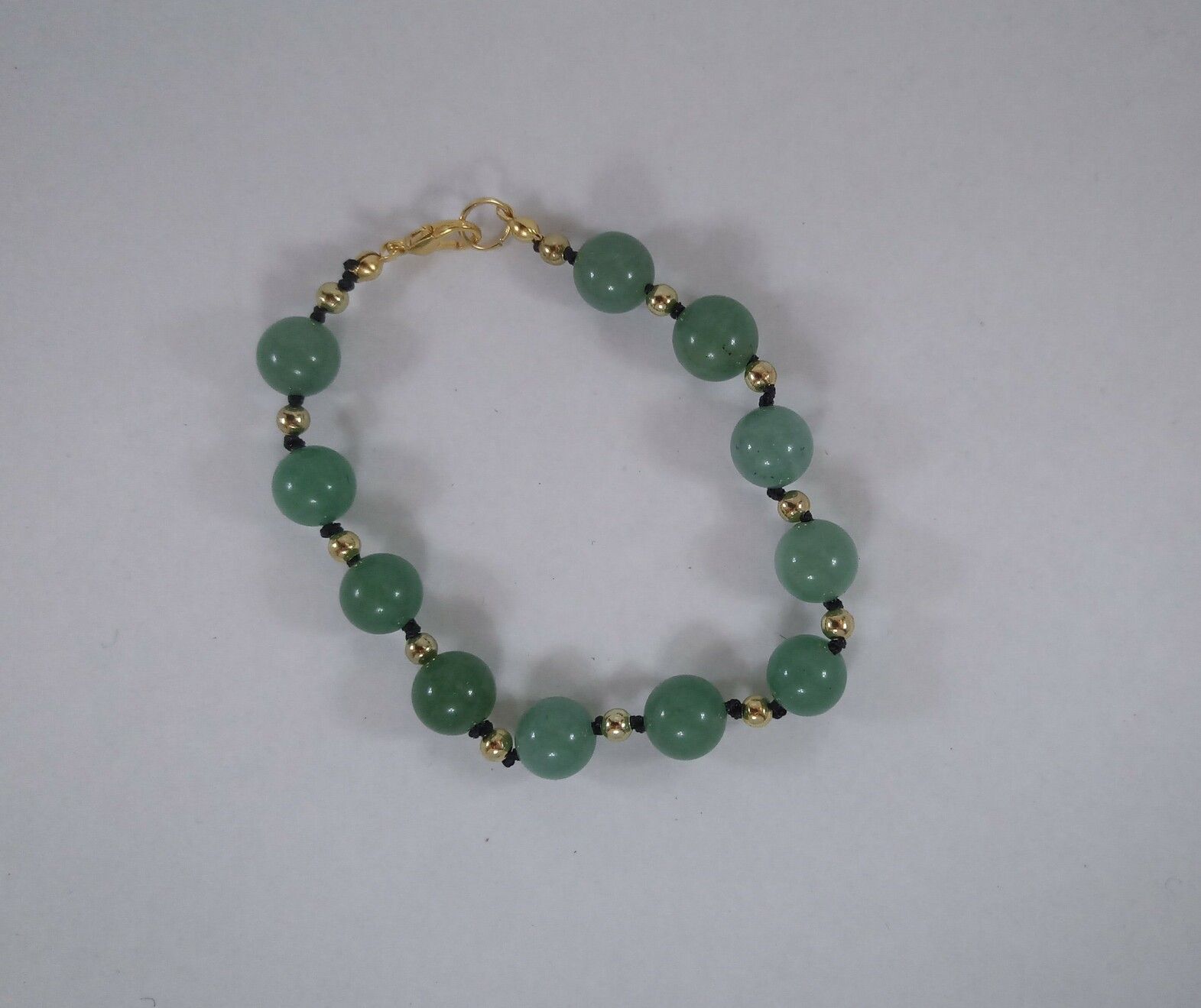 A green aventurine bracelet, strung on black nylon cord with gold spacer beads. Aventurine has a sort of metallic sheen/shimmer to it, which comes out silvery in the green variety. The green stones range from a pale sage to a fairly deep forest green. 