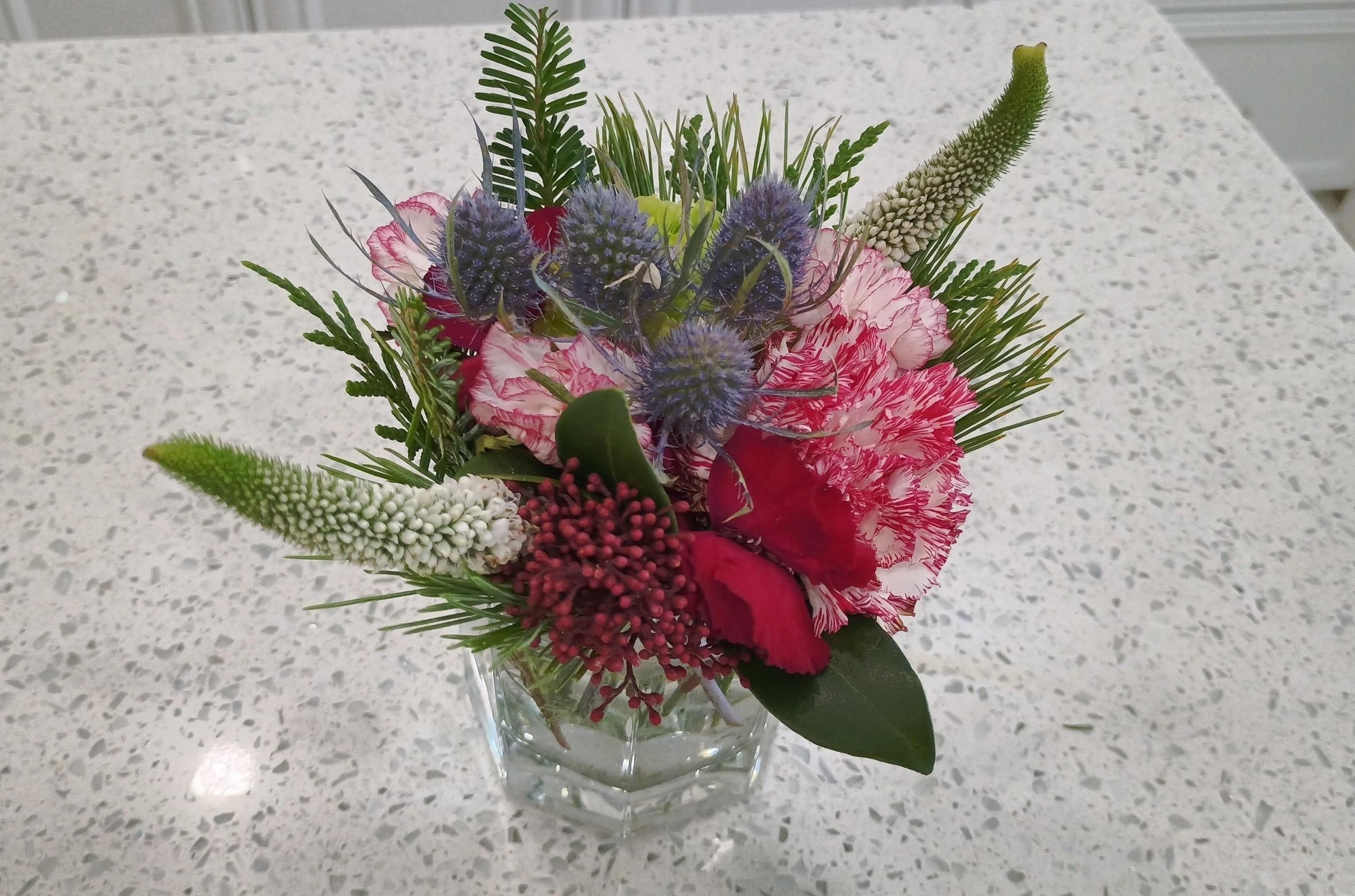 A small pretty floral arrangement features a variety of shapes and colours in the green, red, blue, and white space. It's a bit spikey and a little alien looking.