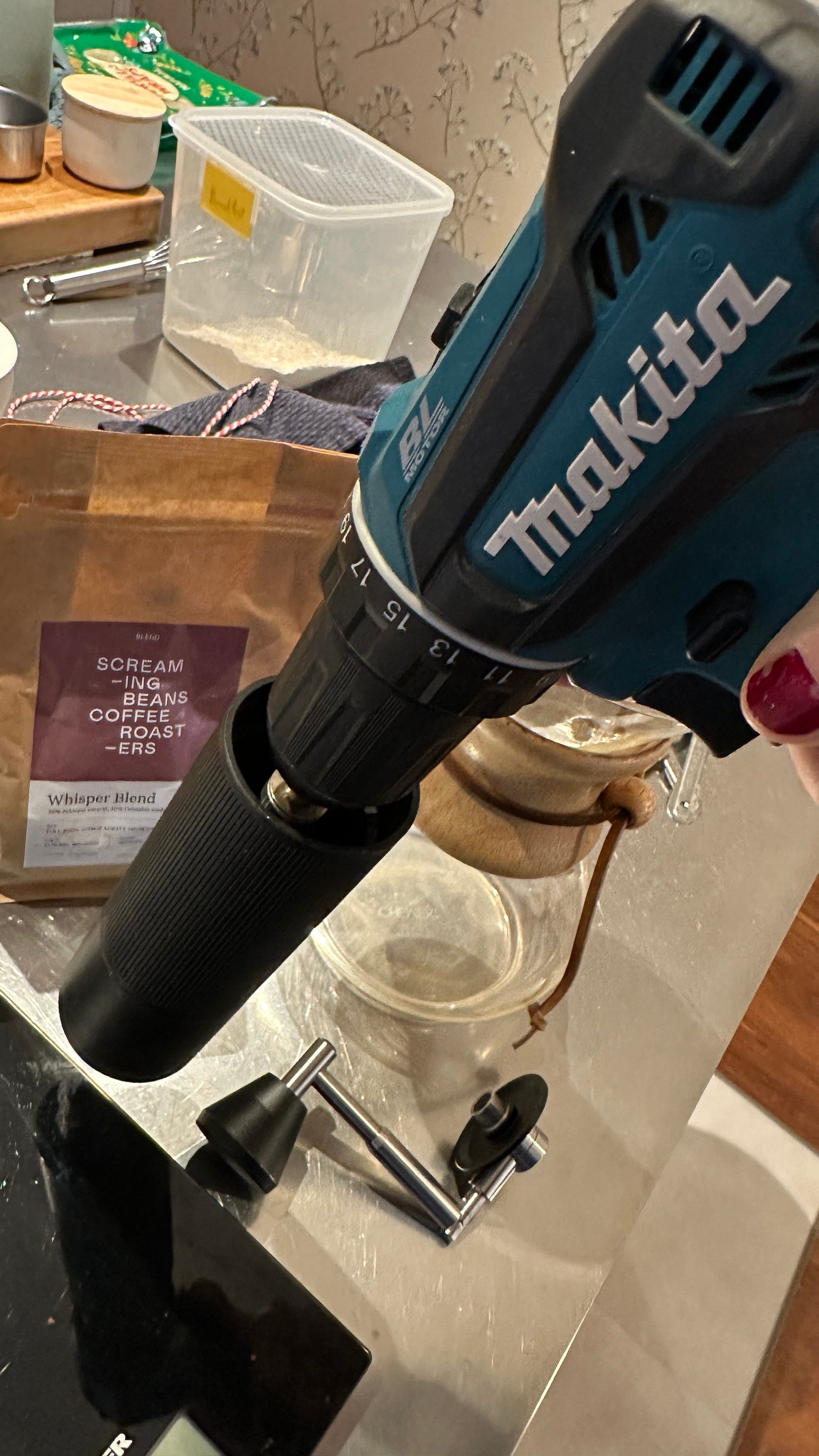 Hand coffee mill chucked to a Makita power drill. Various kitchen stuff is in the background. 