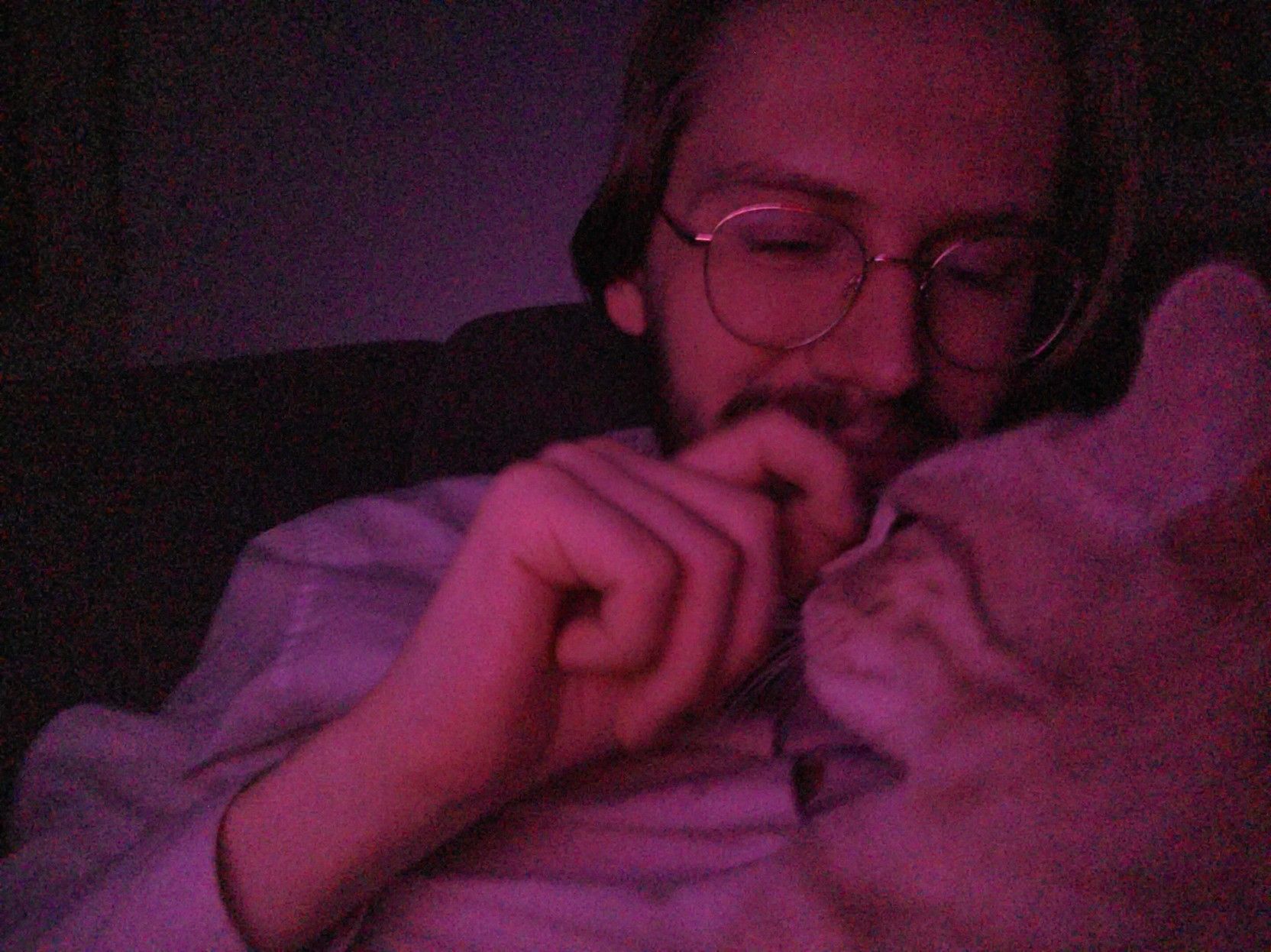 A picture of Erik Uden petting the little cat named Lenin on his nose whilst he's lying on his stomach and they're being illuminated by red light