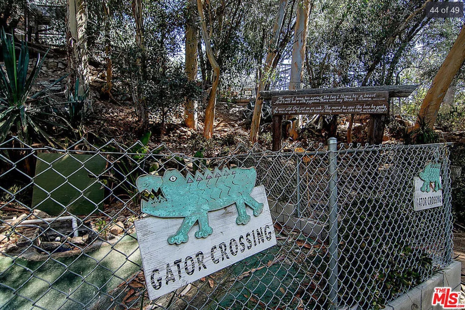 A sign that says Gator Crossing, it is crudely made out of wood and on a chain link fence. 