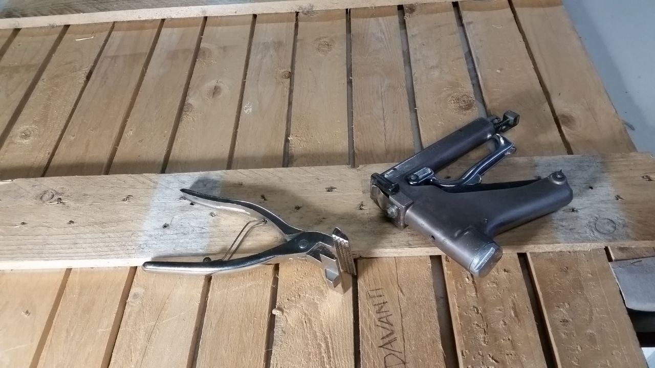 Pinza tira tela (anche tendi tela, su qualche sito) a fianco di una spara graffette pesantissima, che immagino sia in ghisa.
Gli attrezzi sono appoggiati sul retro della pedana bassa del tavolo semovente.