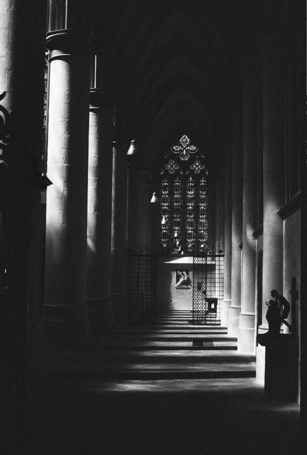 The aisle of a Gothic abbey. Pillars and statues are cast in stark black and white.