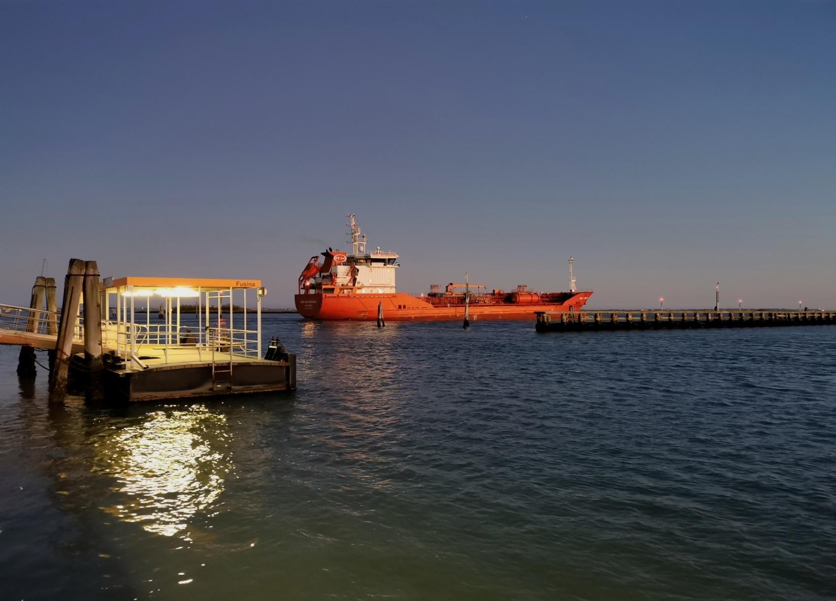 Foto di un approdo per vaporetti a Fusina, Venezia. Sullo sfondo c'è il canale dei Petroli, dove passa una nave da carico.