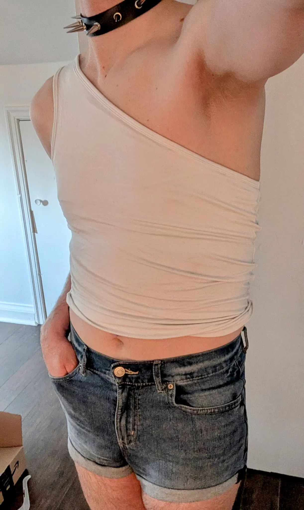 I stand causally for this selfie, and in the pockets of my short jean shorts. I'm wearing a white asymmetrical shirt, and my midriff is visible. 
On my neck I'd a spiked collar