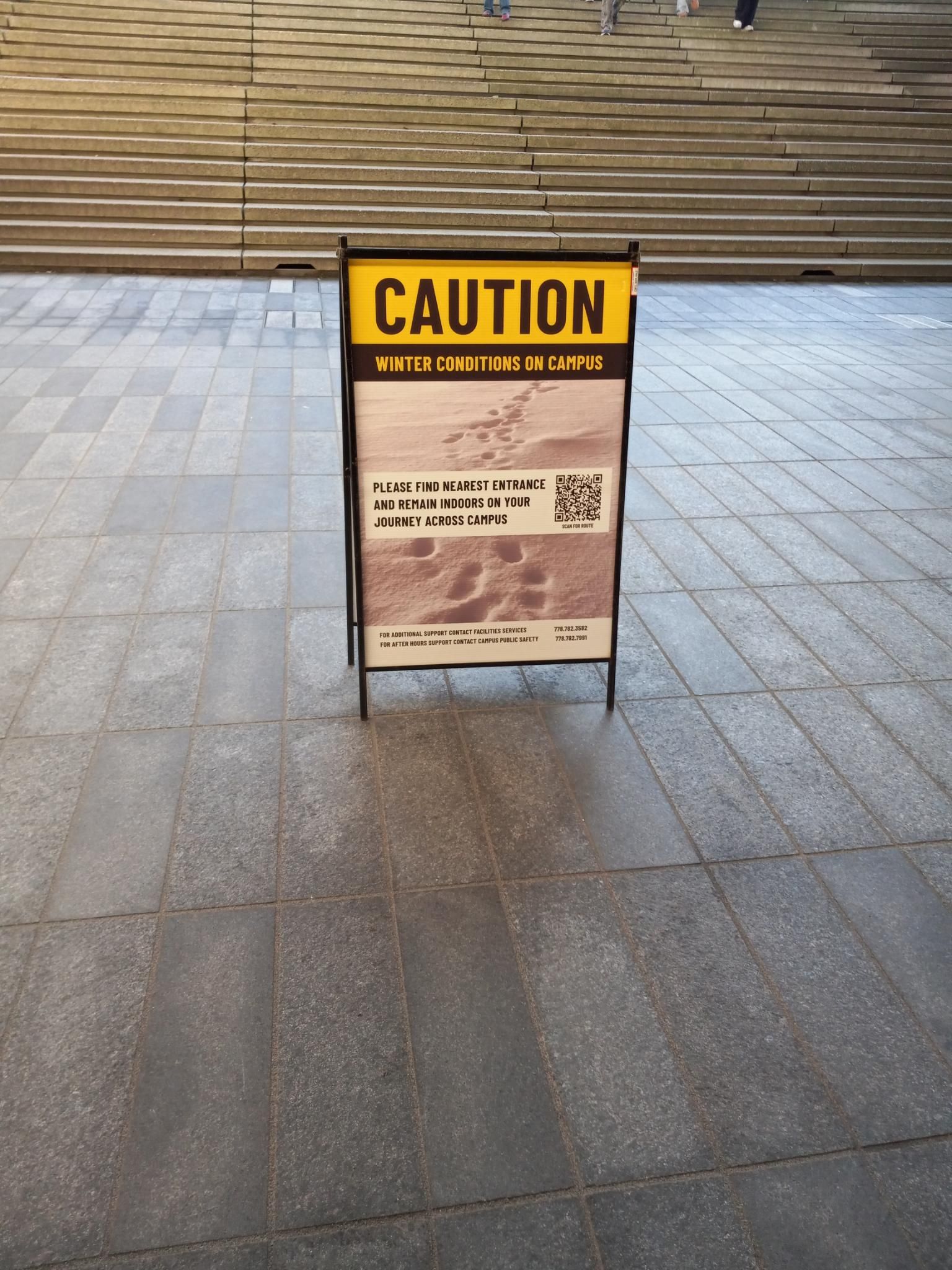 A sign standing on a walkway that says "PLEASE FIND NEAREST ENTRANCE AND REMAIN INDOORS ON YOUR JOURNEY ACROSS CAMPUS".  It was maybe -2C and there was a teeny tiny bit of frost in a few places.