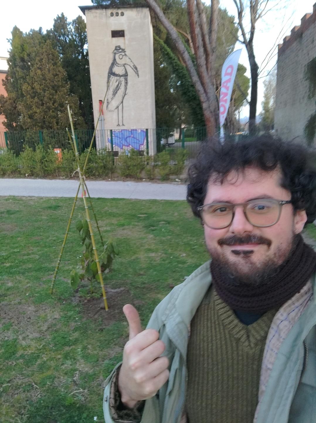 Gabriele Primavera Dani un cannicciato che protegge un Avocado di 5 anni. Sullo sfondo, su una cabina elettrica, un murale che raffigura un uccello con una maschera da medico della peste.