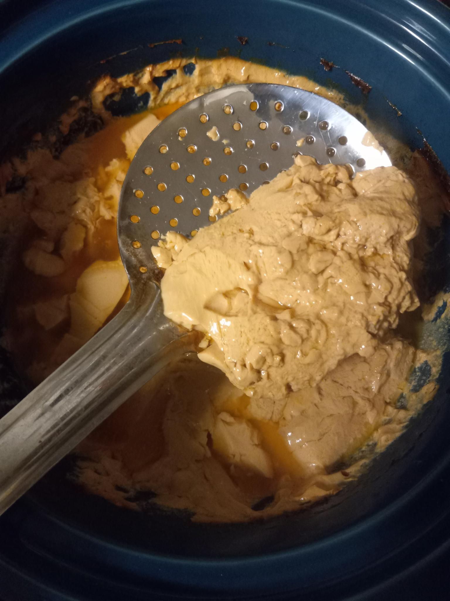 The same ceramic pot, now with the baked crusty milk layer removed, and a ladle picking up some of the baked, caramel coloured milk, highlighting its weird jello-like consistency. 