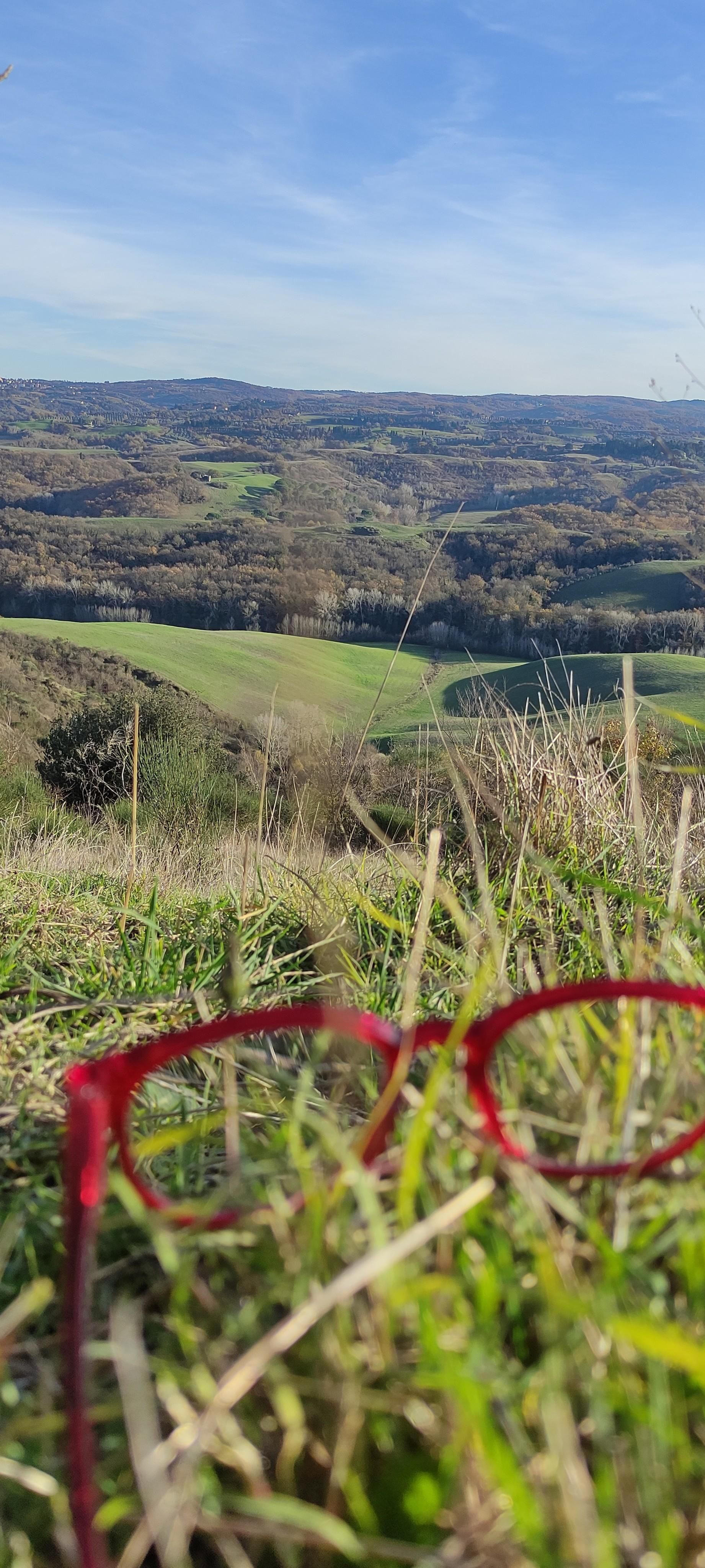panorama collinare, occhiali rossi in primo piano appoggiati sull'erba