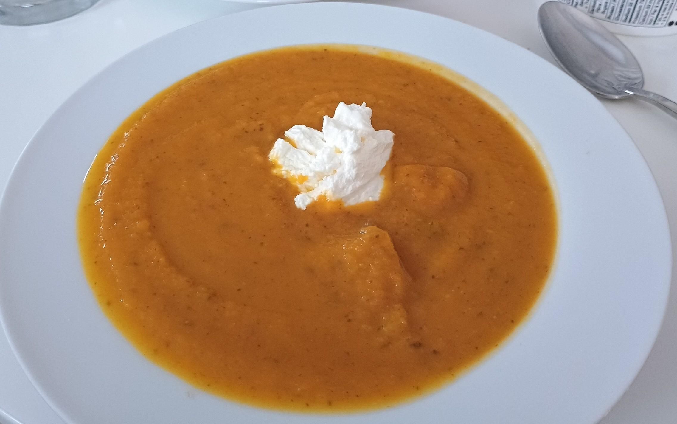 An orange thick soup in a white bowl with a glob of white thick sour cream in the middle