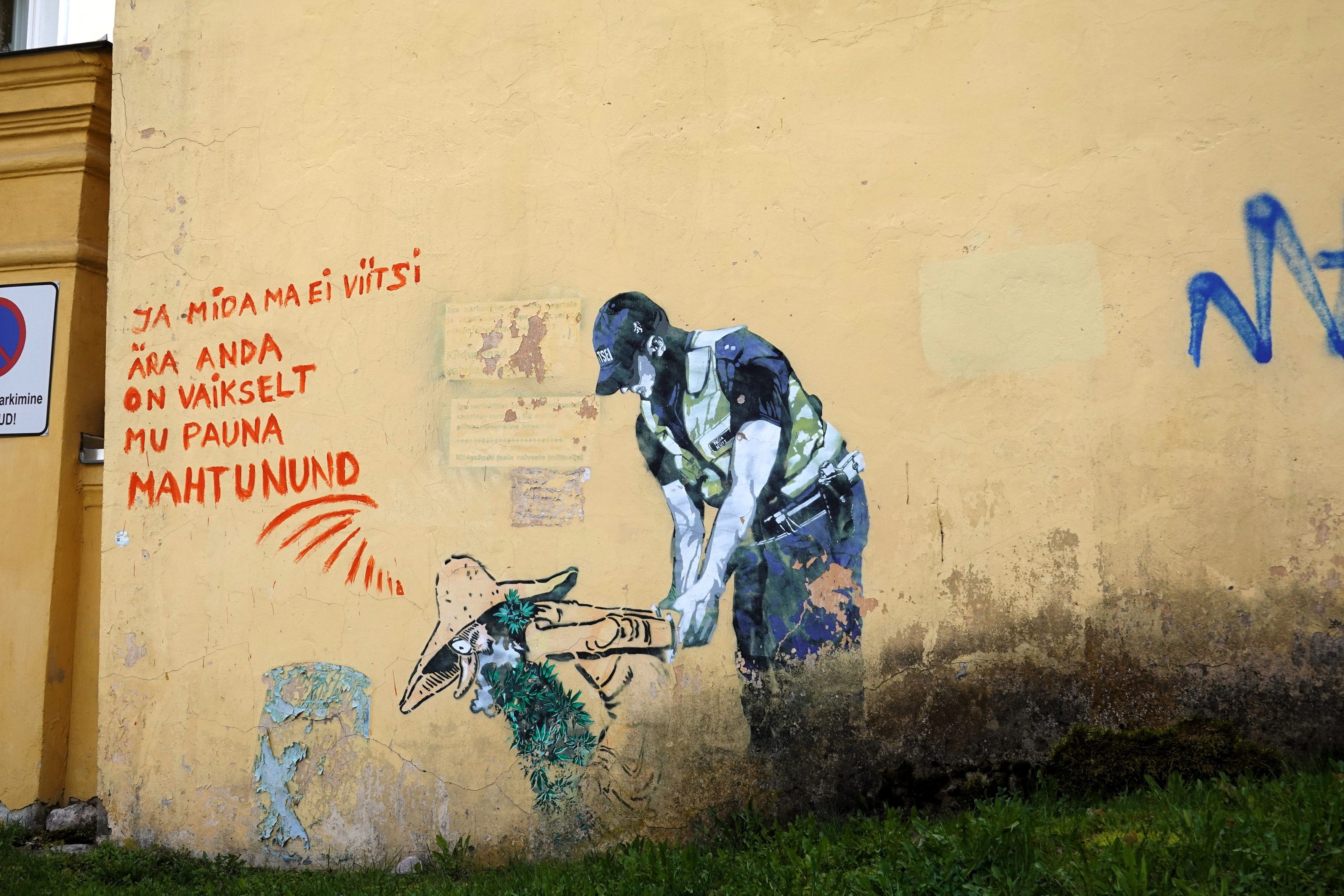 Street art in Estonia with some mythical creature being led away in cuffs and some words on the wall.